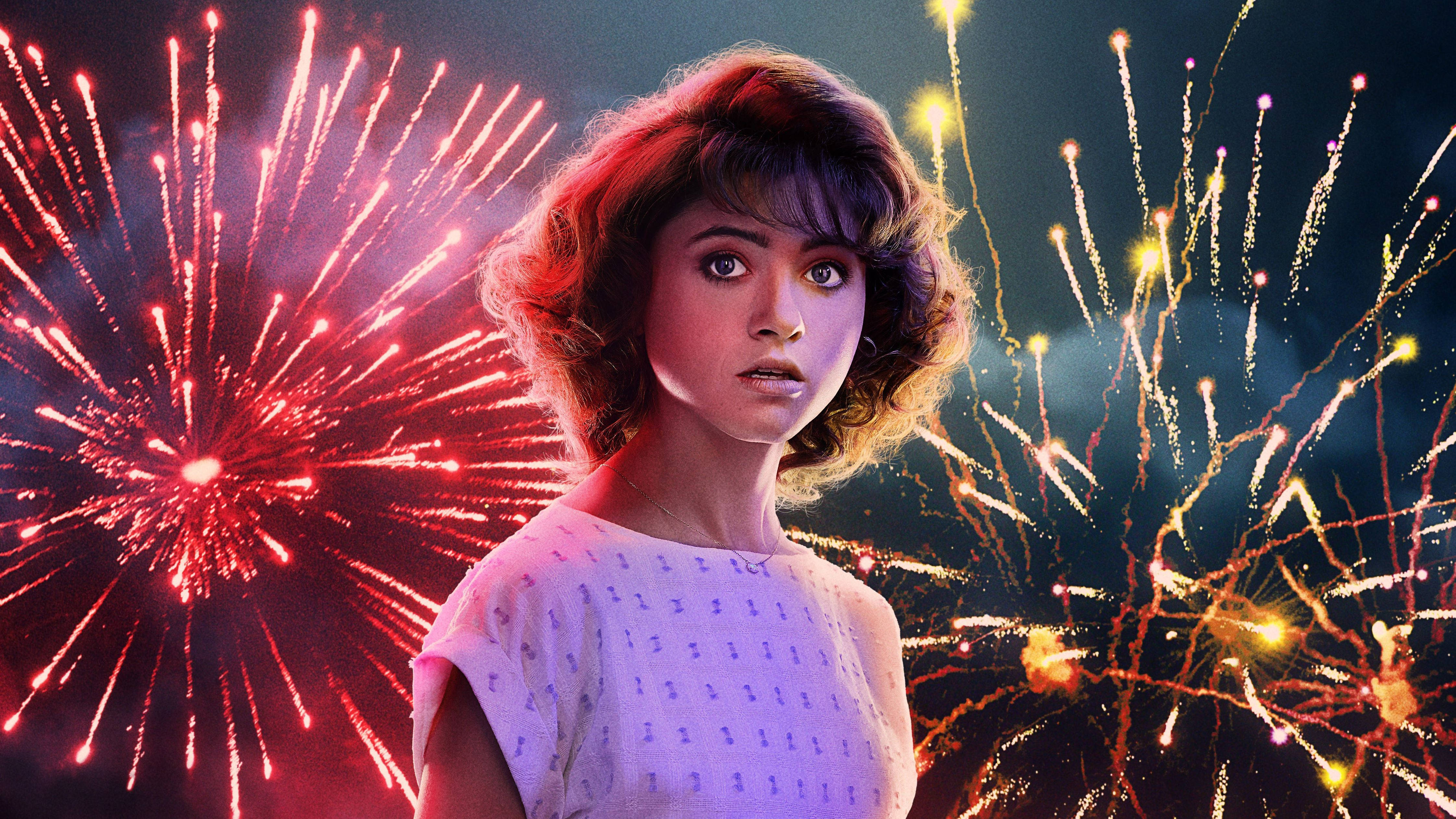 Stranger Things 3 桌布 壁紙 — 一位年輕的捲髮女性直視前方，身後有鮮豔的紅色和金色煙火在黑暗的天空中爆炸。