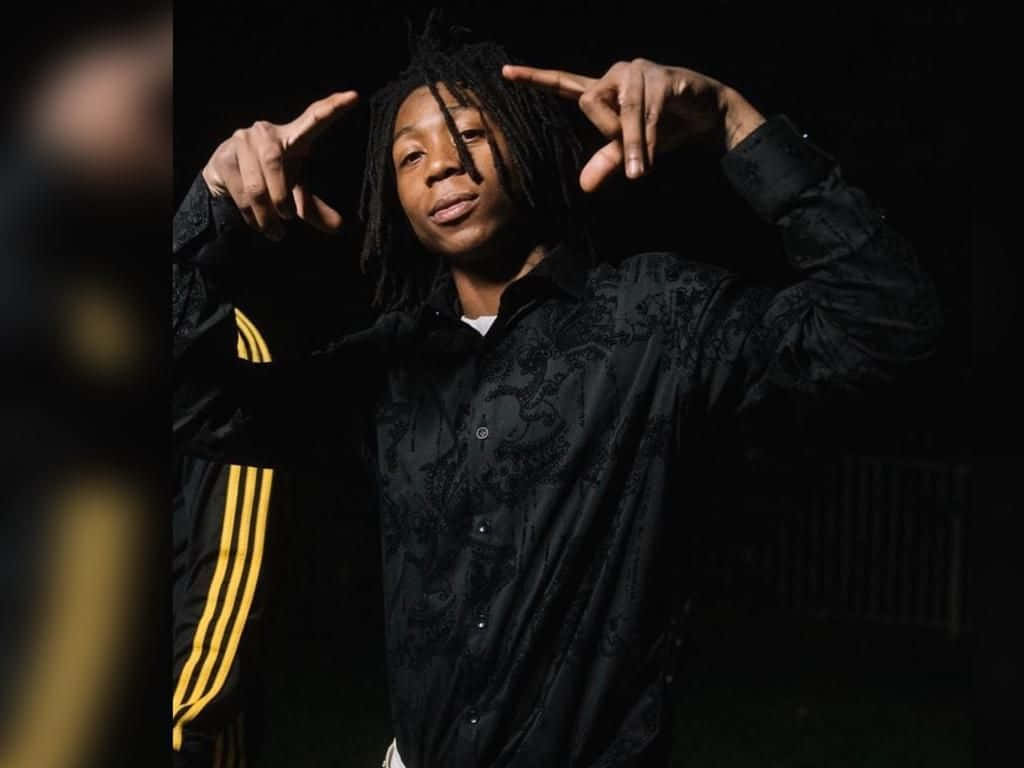 Dead Rappers 桌布 壁紙 — 一位年輕的辮子男在昏暗的肖像照中指向自己的頭部，身穿帶有黃色條紋的黑色圖案外套。