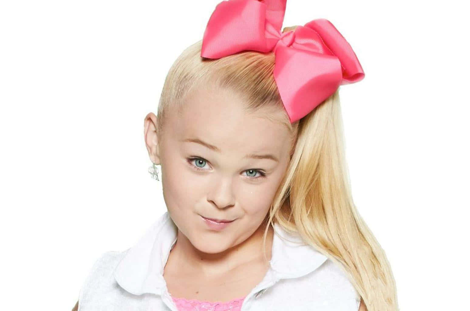 JoJo Siwa 桌布 壁紙 — 一位年輕的金髮藍眼女孩，在白色背景前，頭髮上戴著一個大粉紅色蝴蝶結，身穿白色有領襯衫。