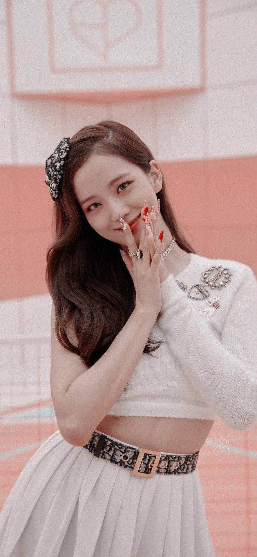 Jisoo Cute 桌布 壁紙 — 一位年輕的長髮棕髮女性，在柔和的粉紅色瓷磚牆前，用塗有顏料的手指輕觸嘴唇，溫柔地微笑。
