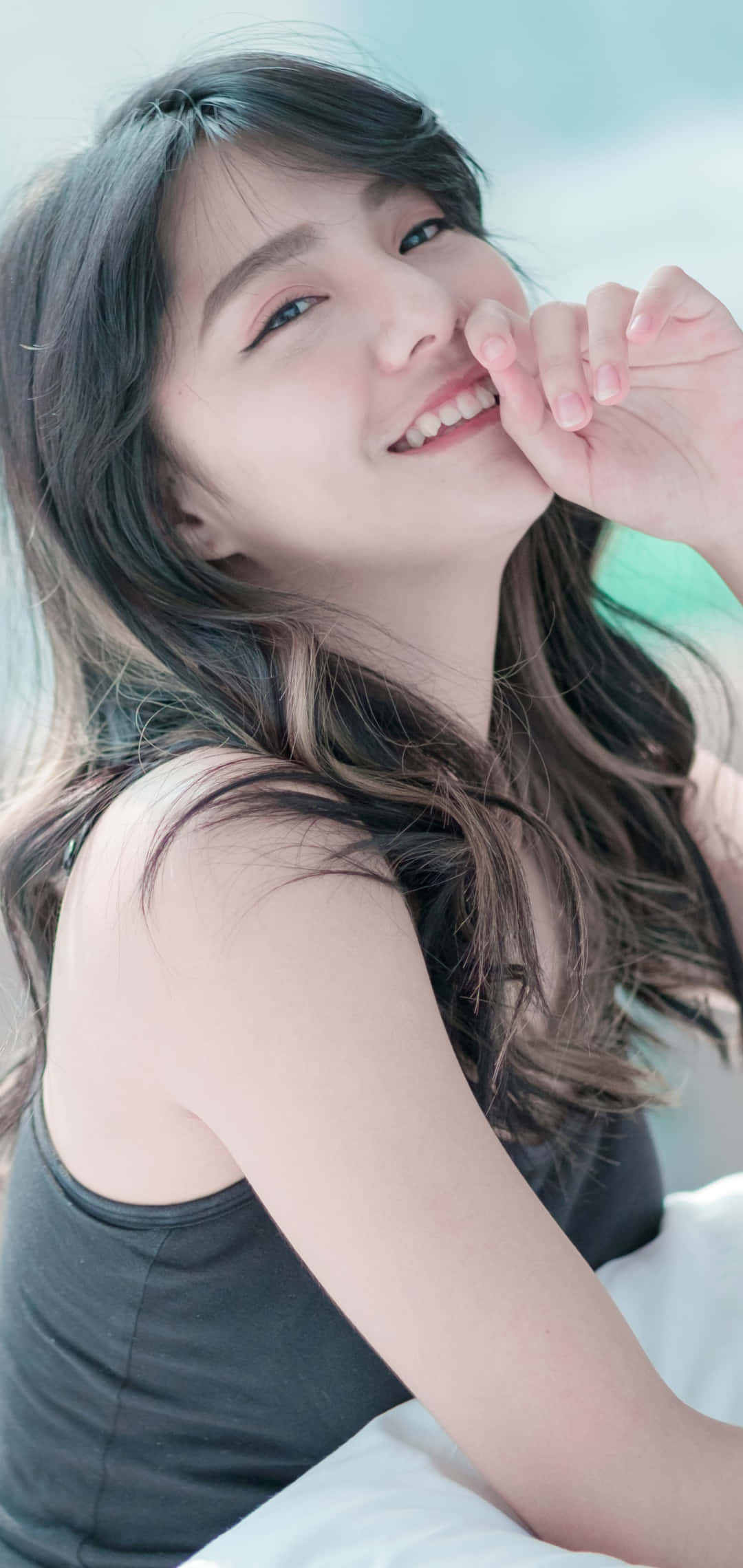 Cute Girl 桌布 壁紙 — 一位年輕的長黑髮女性，在柔和的模糊背景上，輕輕地將下巴靠在手上微笑。