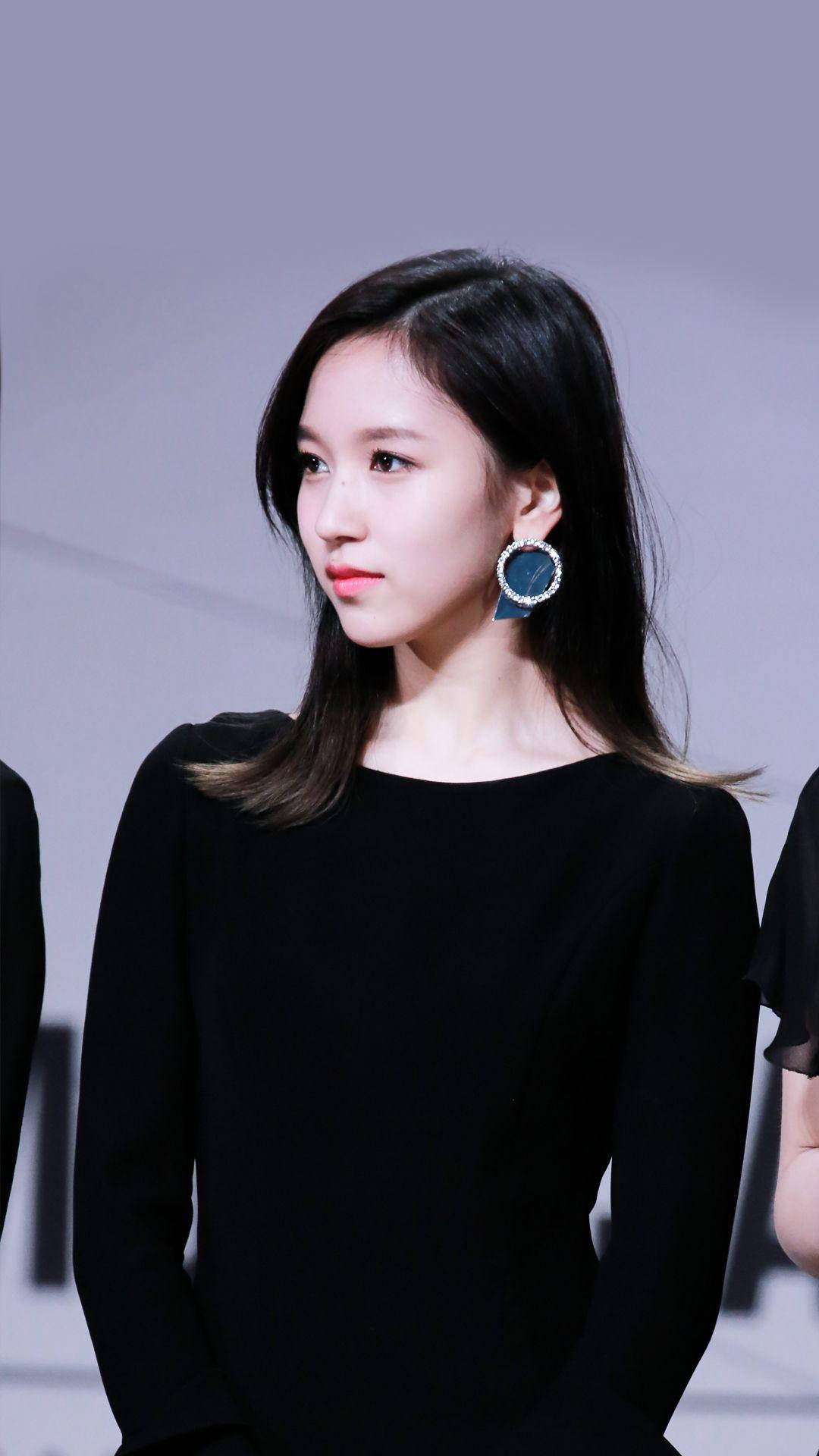 Kpop Aesthetic 桌布 壁紙 — 一位年輕的長黑髮女性，穿著黑色上衣，戴著大顆藍寶石耳環，背景是純灰色。