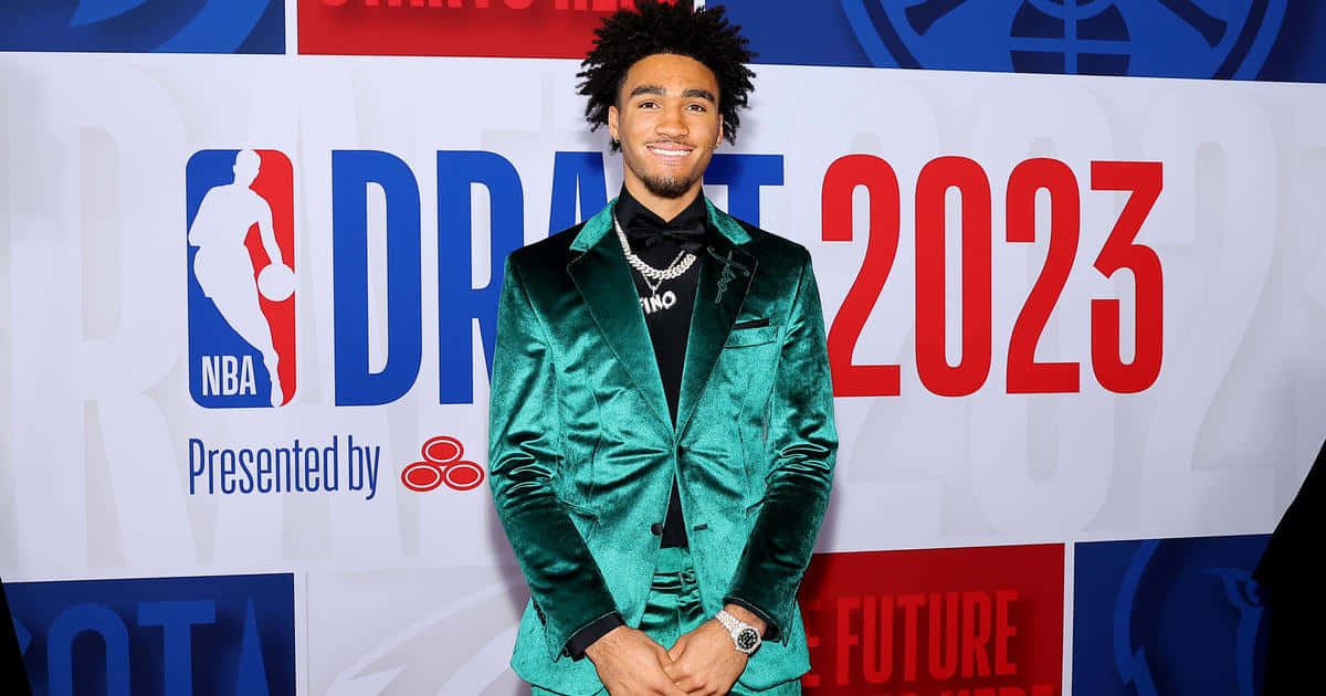  壁紙 — 一位年輕籃球運動員穿著閃亮的綠色天鵝絨西裝，在NBA選秀2023活動背景下自信地微笑。