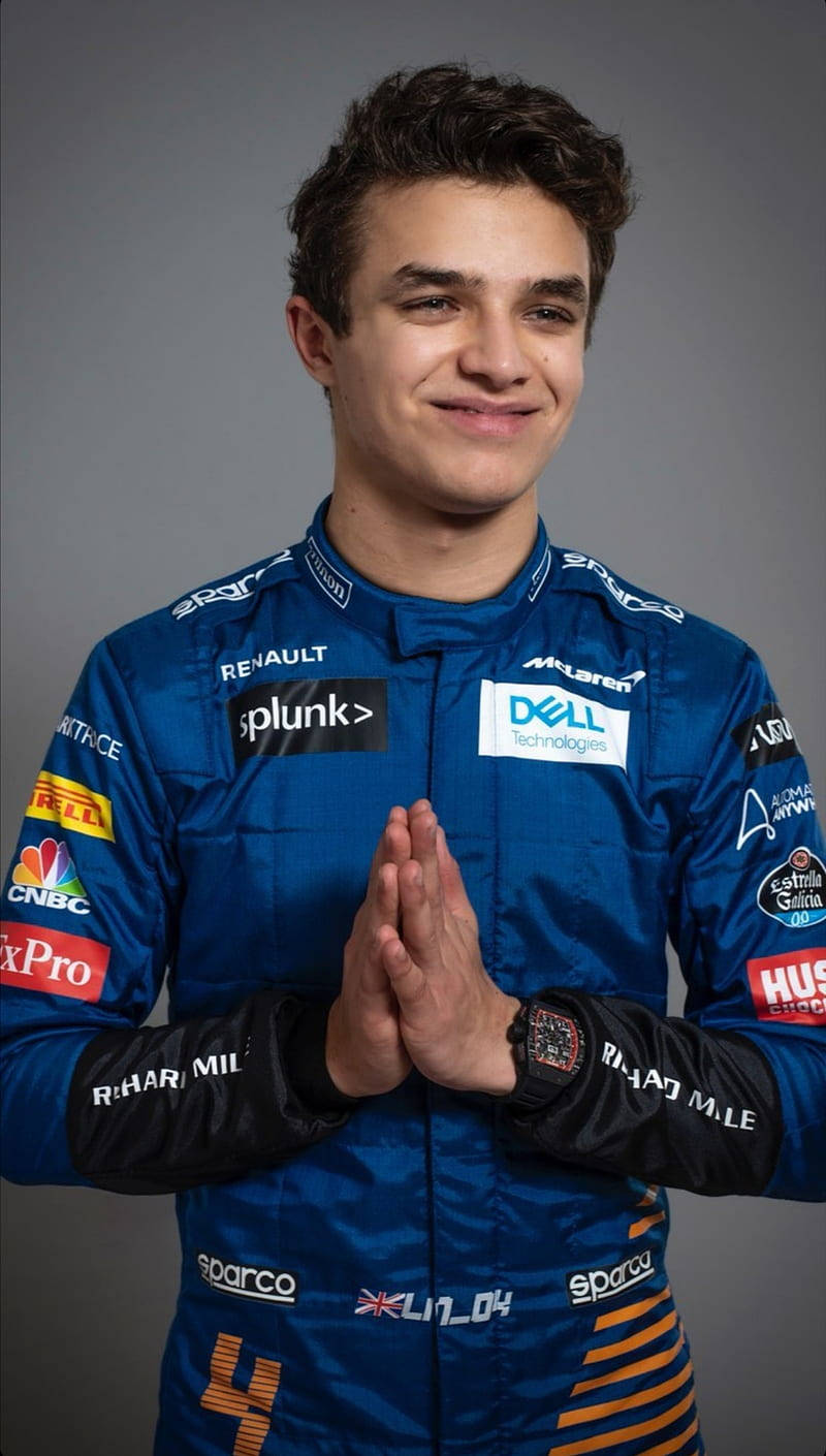 Racing 桌布 壁紙 — 一位年輕賽車手身穿藍色McLaren賽車服，在純灰色背景前雙手合十，溫暖地微笑。