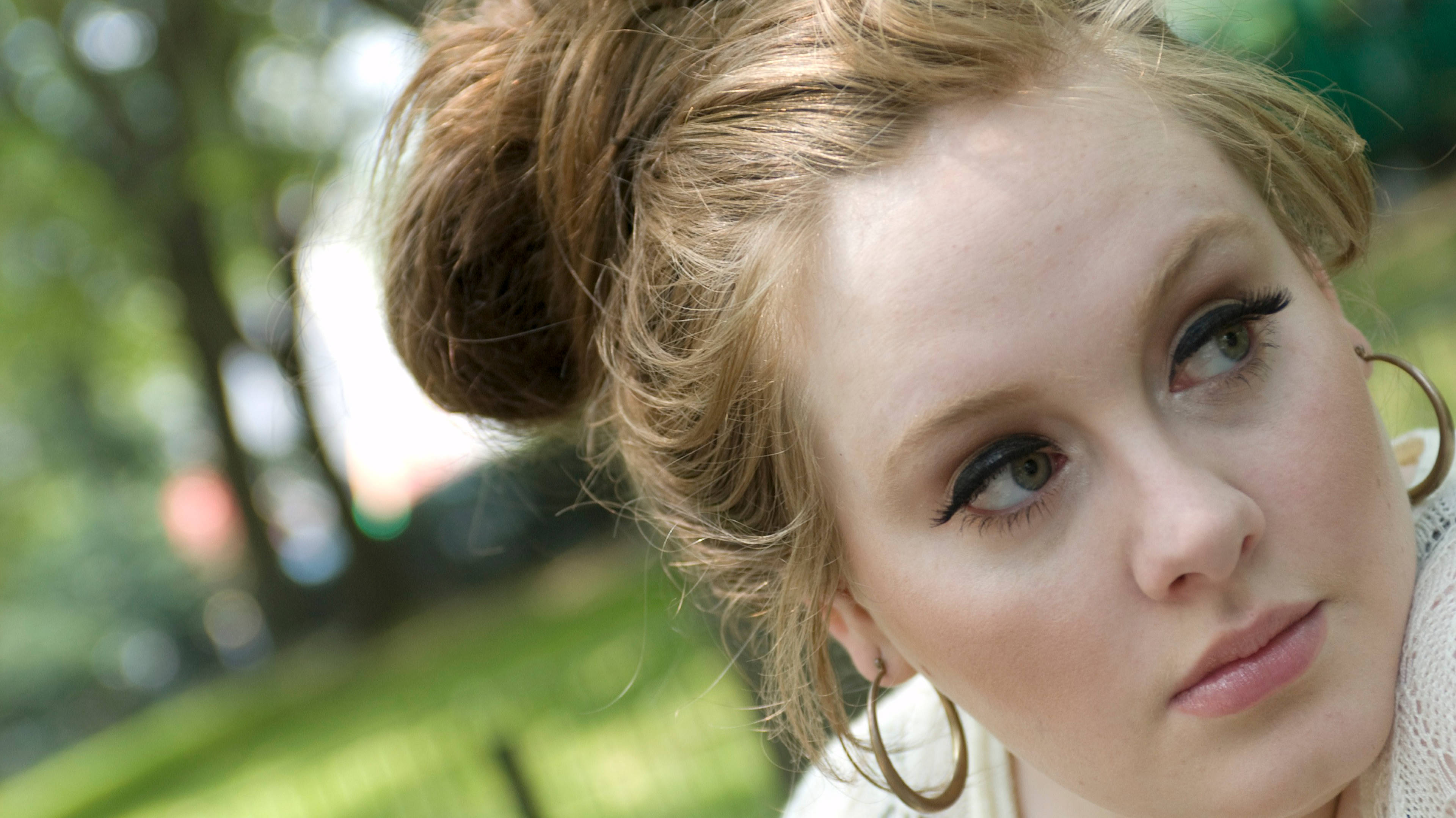 Adele 桌布 壁紙 — 一位年輕金髮女性的近距離肖像，頭髮紮成凌亂的髮髻，戴著大圈耳環，在戶外若有所思地凝視。