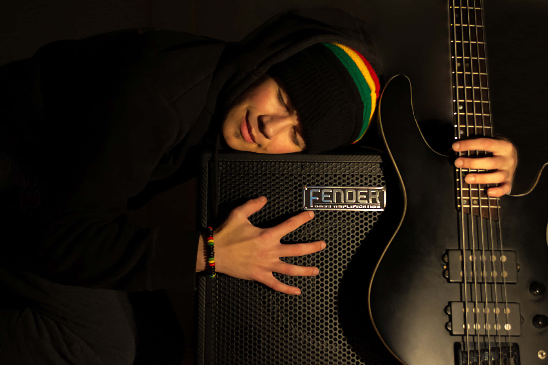 Bass Guitar 桌布 壁紙 — 一位年輕音樂家將頭靠在Fender擴音器上，同時在昏暗的錄音室裡拿著一把黑色電吉他。