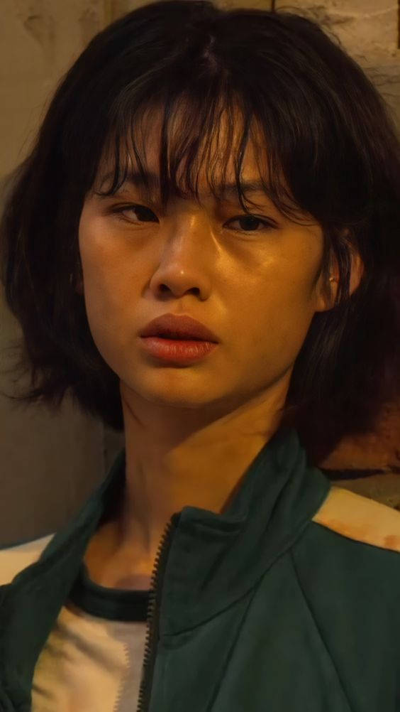 桌布 壁紙 — 一位年輕黑髮女子穿著綠色外套，在溫暖昏暗燈光下的特寫肖像。