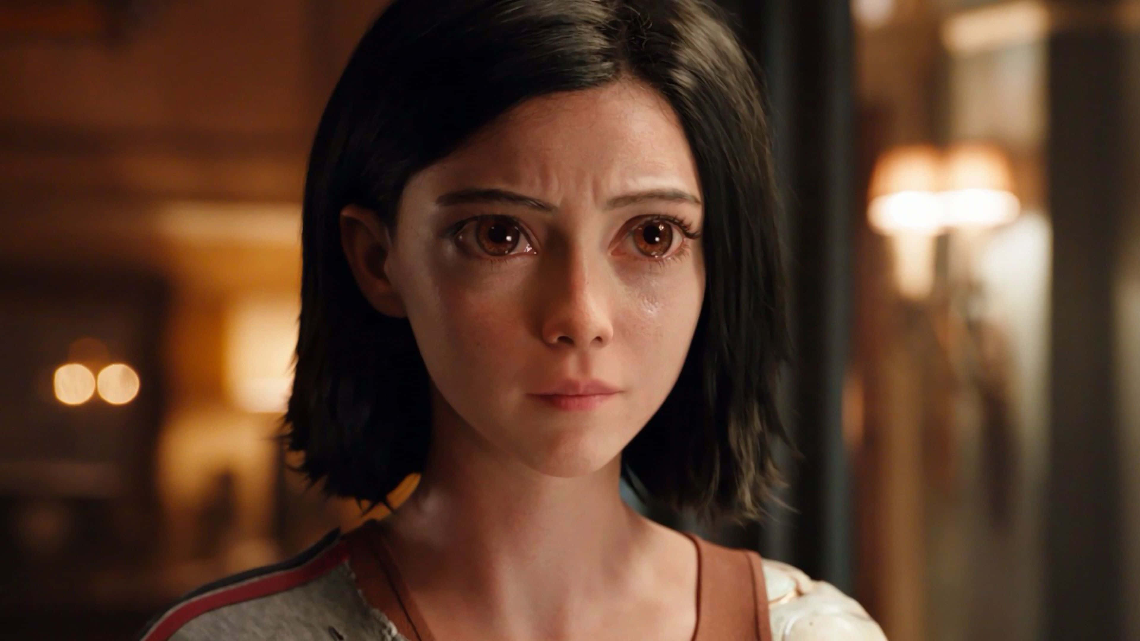Alita Battle Angel 桌布 壁紙 — 一位年輕黑髮女性的特寫，她雙眼充滿淚水，在溫暖燈光的室內環境中向前凝視。