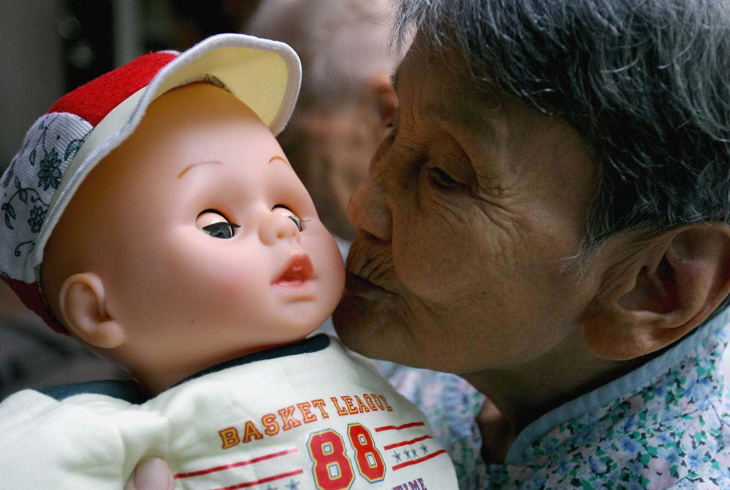 Doll 桌布 壁紙 — 一位年長女性溫柔地親吻一個戴著紅白帽子和穿著「Basket League 88」襯衫的嬰兒娃娃。