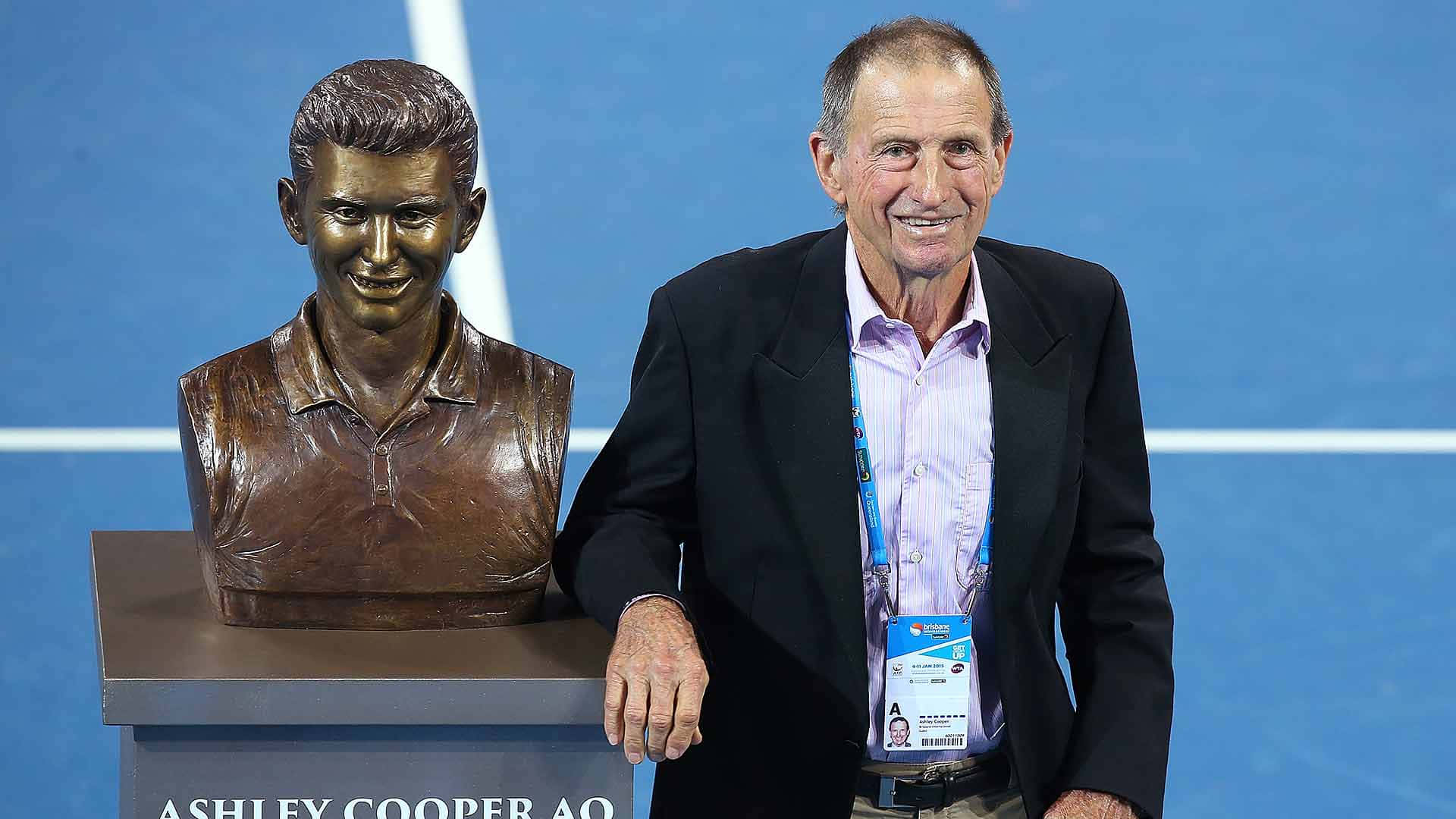 Ashley Cooper 桌布 壁紙 — 一位年長男士在藍色網球場的基座上，微笑站在自己的銅像半身像旁邊。