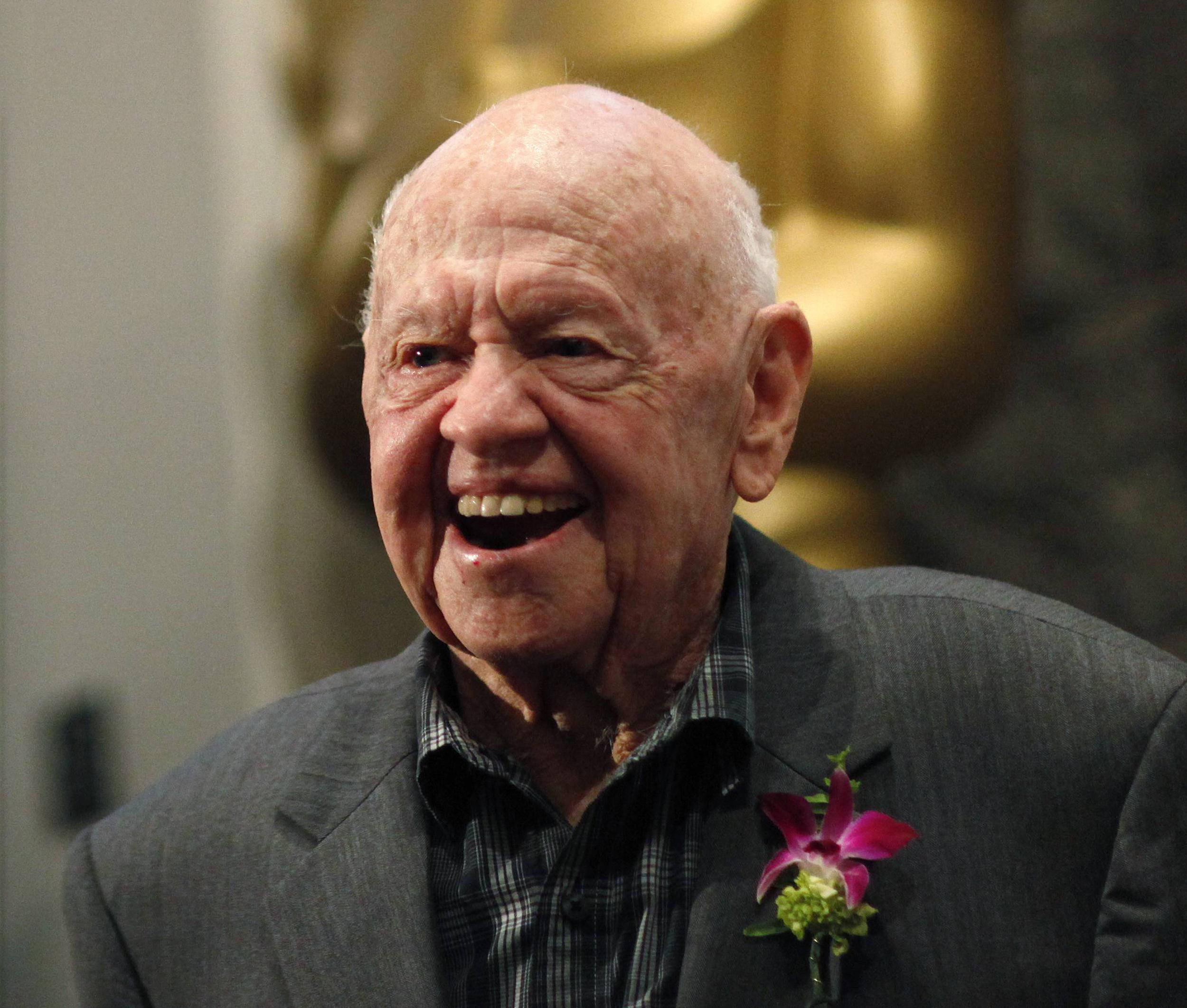 mickey rooney 桌布 壁紙 — 一位年長男士帶著愉快的笑容，身穿灰色西裝，佩戴紫色蘭花胸花。