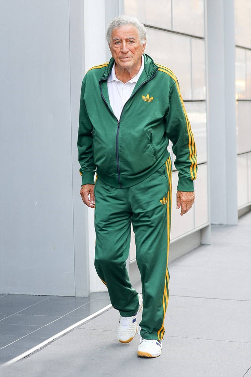 actor 桌布 壁紙 — 一位年長男性自信地穿著綠色Adidas運動服（帶黃色條紋）走過現代玻璃建築外牆。