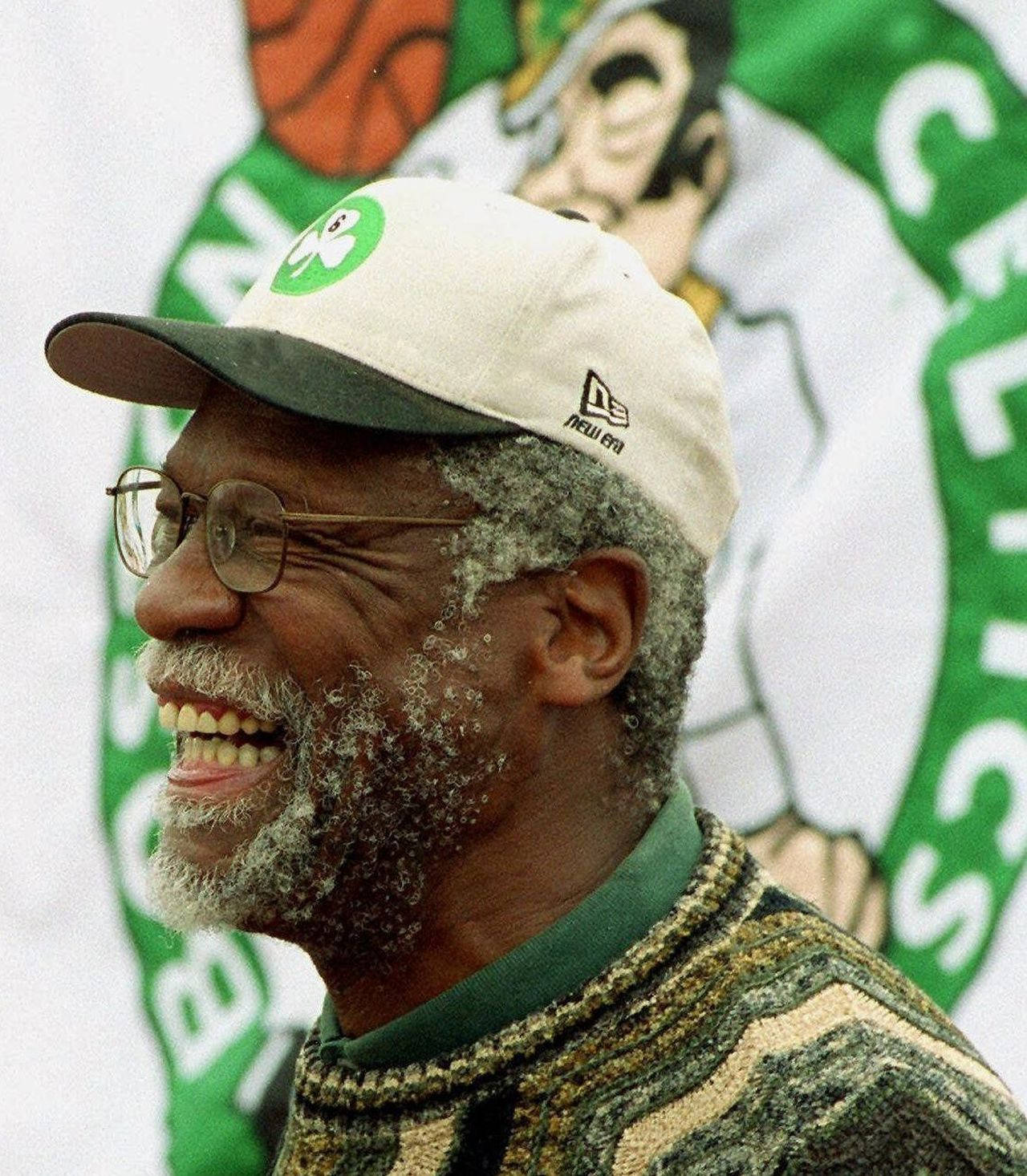 Boston Celtics 桌布 壁紙 — 一位年長的黑人男子，帶著喜悅的笑容和眼鏡，戴著塞爾提克隊的帽子，背景是球隊標誌。