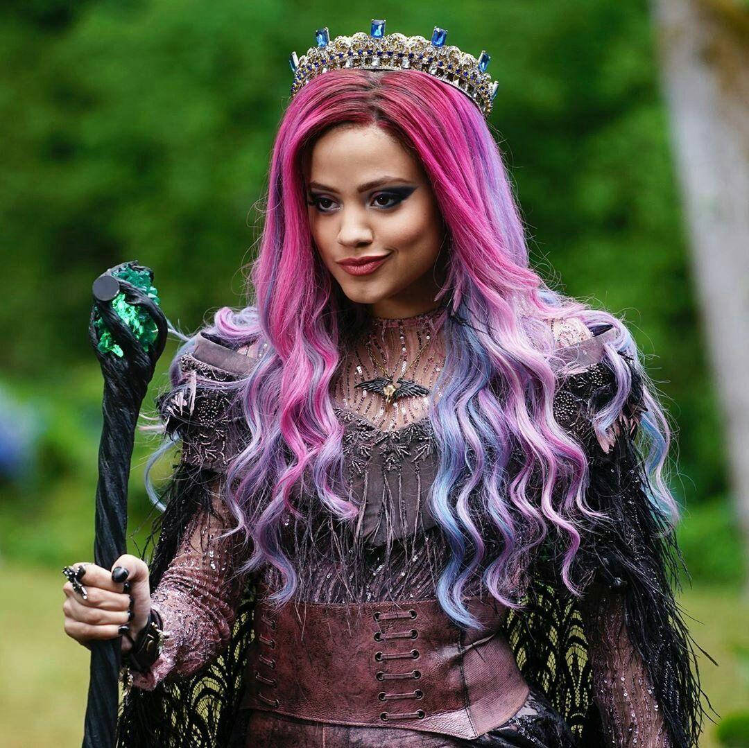 Descendants 桌布 壁紙 — 一位幻想女王，擁有充滿活力的粉紅色、紫色和藍色頭髮，戴著鑲有寶石的王冠，在茂密的綠意中手持發光的綠色法杖。