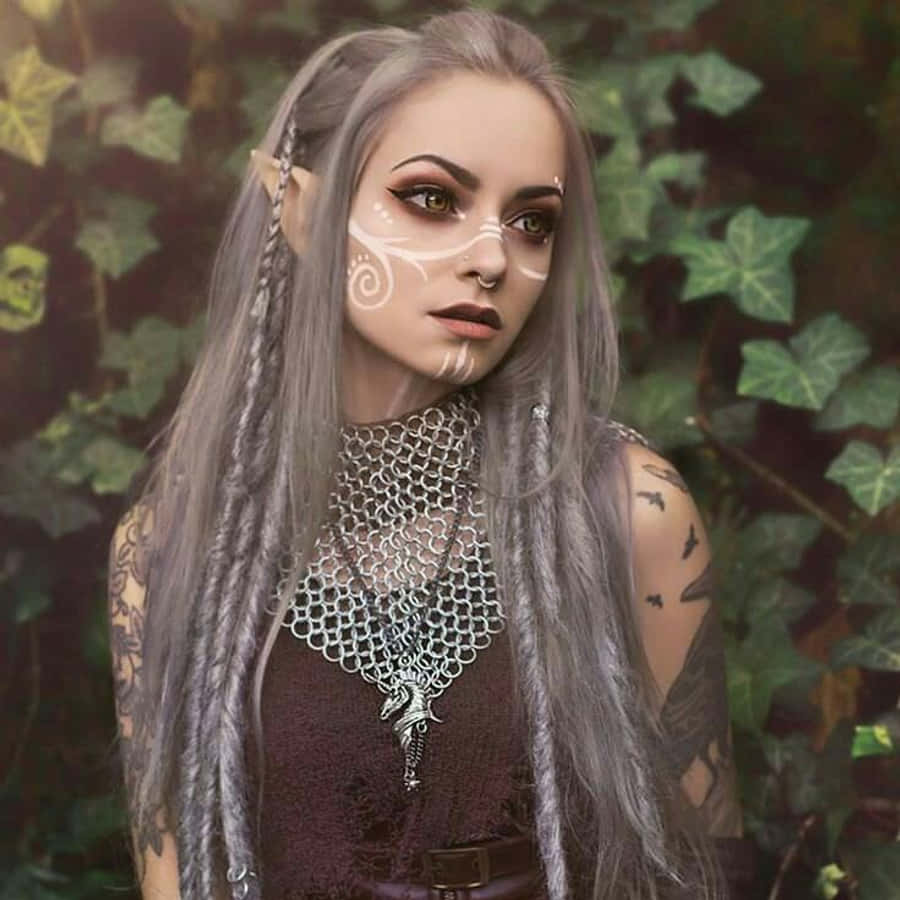 Real Elf 桌布 壁紙 — 一位幻想精靈女性，銀色頭髮和臉部彩繪，身處茂密的綠色常春藤中，穿著鎖子甲和紋身。