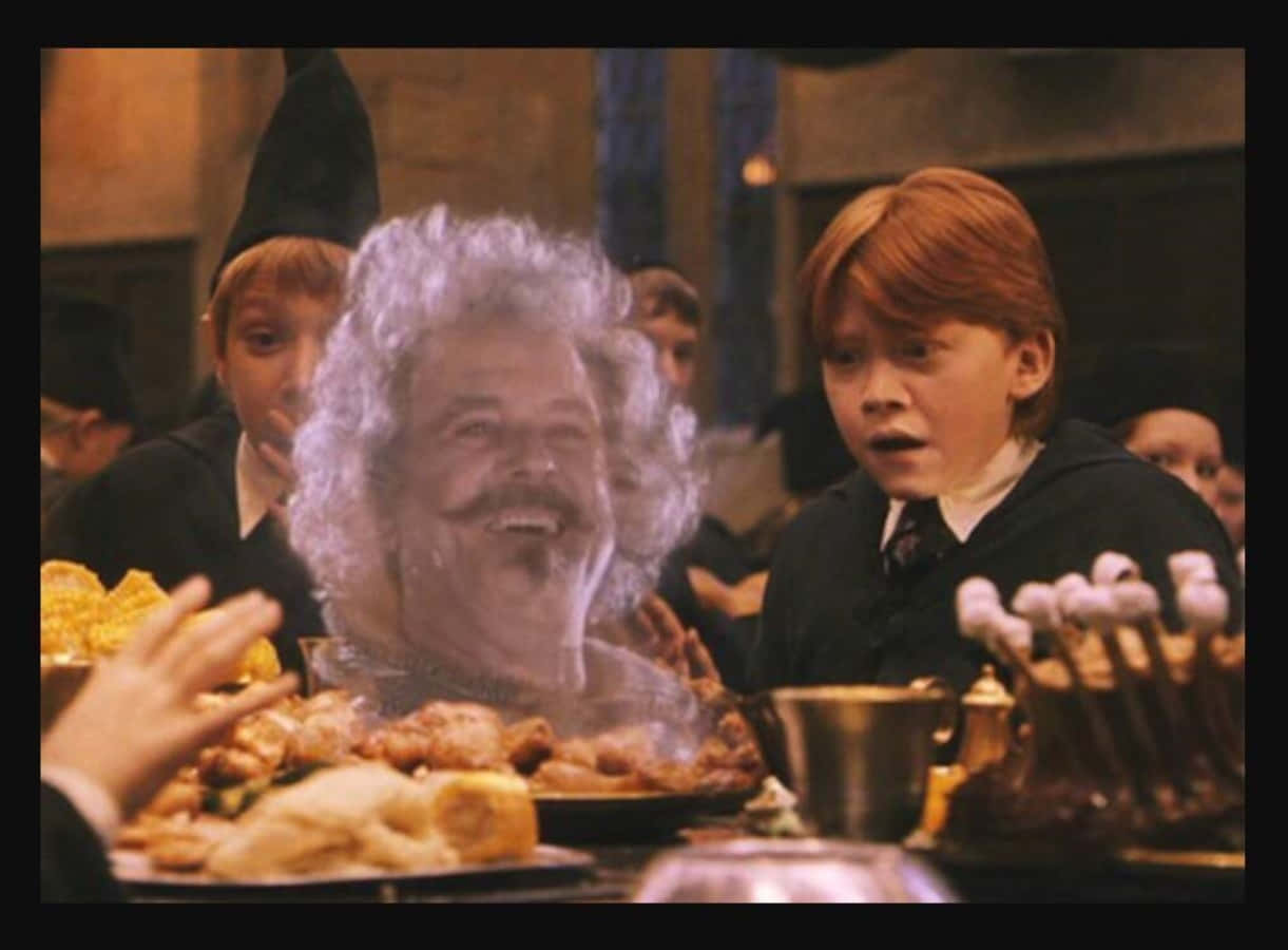 The Hogwarts Ghosts 桌布 壁紙 — 一位幽靈教授，白色頭髮和鬍鬚蓬鬆，漂浮在宴會桌上，而一個年輕的紅髮男孩震驚地凝視著。