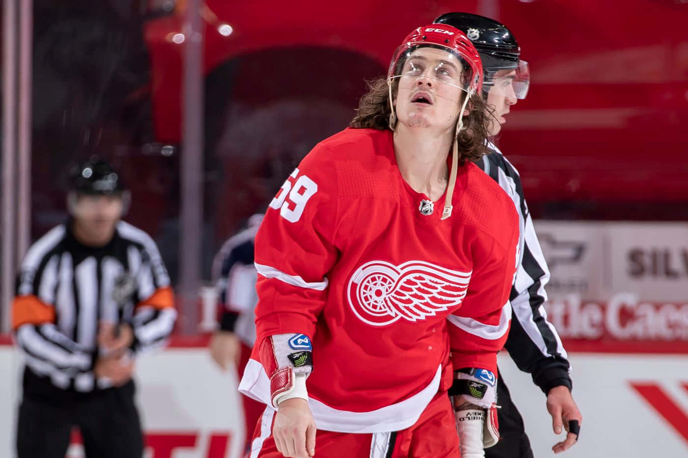Tyler Bertuzzi 桌布 壁紙 — 一位底特律紅翼隊的冰球運動員身穿紅色59號球衣，在裁判附近比賽時，強烈地向上看。
