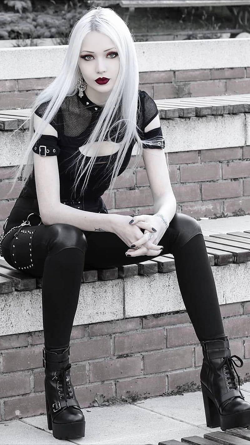 女孩 桌布 壁紙 — 一位引人注目的哥德式女性，擁有白金髮色和大膽的紅唇，在單色調的磚牆上優雅地坐著。