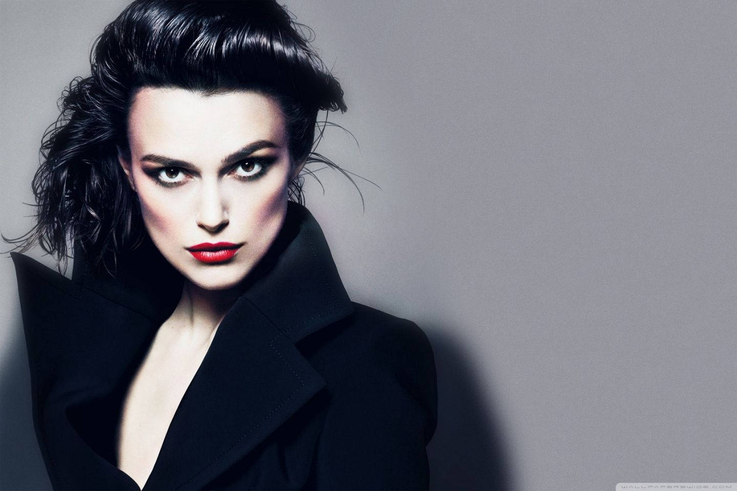 Keira Knightley 桌布 壁紙 — 一位引人注目的女性，擁有鮮豔的紅唇和戲劇性的妝容，在柔和的灰色背景下強烈凝視。