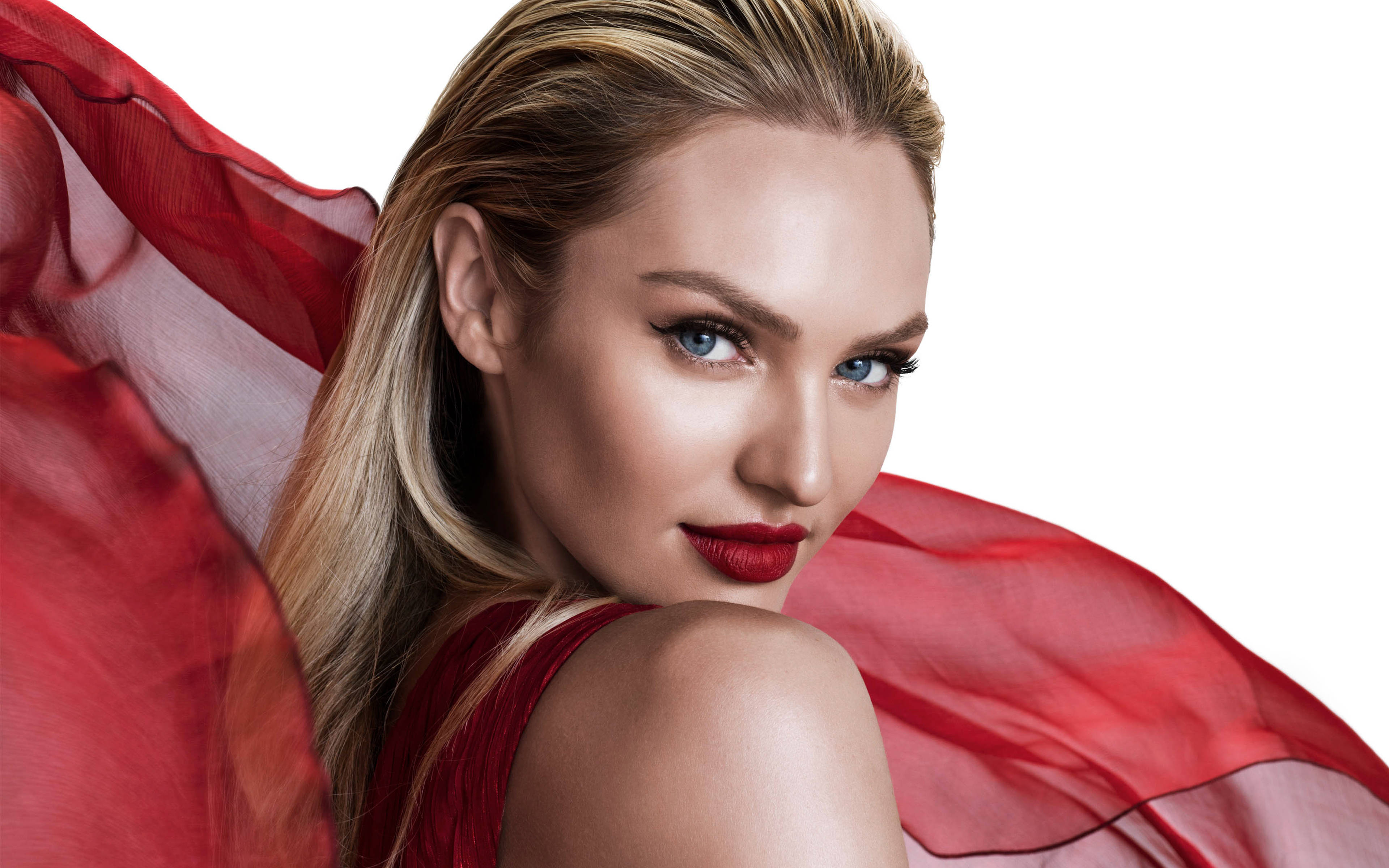 Candice 桌布 壁紙 — 一位引人注目的金髮女郎，擁有鮮豔的紅唇和飄逸的紅色布料，在純白背景前自信地凝視。