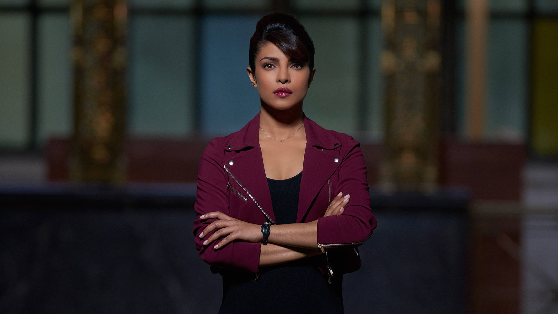 Priyanka 桌布 壁紙 — 一位從容的女性穿著栗色外套，雙臂交叉，背景是模糊的現代室內環境。
