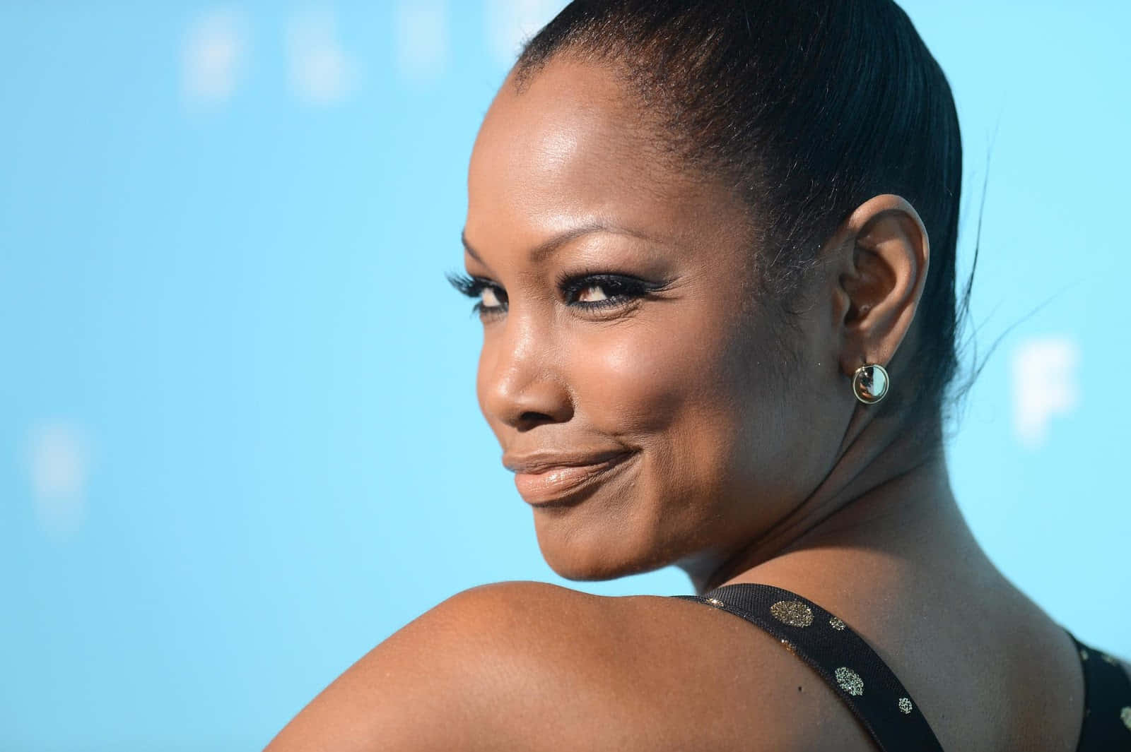 Garcelle Beauvais 桌布 壁紙 — 一位微笑女士的 close-up 肖像，擁有光滑深色頭髮和鮮明眼線，背景為柔和藍色。