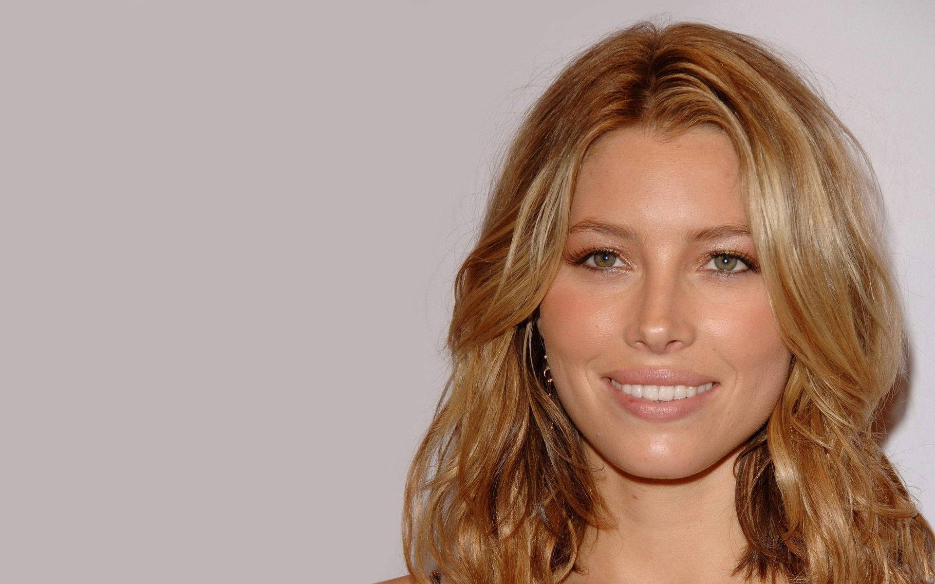 jessica biel 桌布 壁紙 — 一位微笑女士的close-up肖像，擁有波浪形金髮和綠色眼睛，背景為純灰色。
