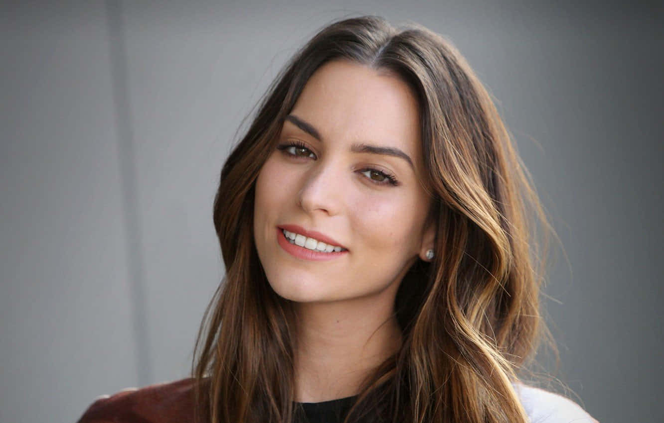 Genesis Rodriguez 桌布 壁紙 — 一位微笑女士的close-up肖像，她擁有長長的棕色頭髮和珍珠耳環，背景是中性灰色。