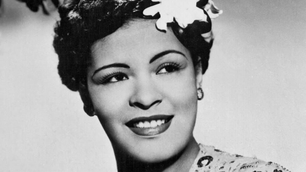 Billie Holiday 桌布 壁紙 — 一位微笑女士的燦爛黑白肖像，頭髮上插著一朵花，戴著優雅的耳環。