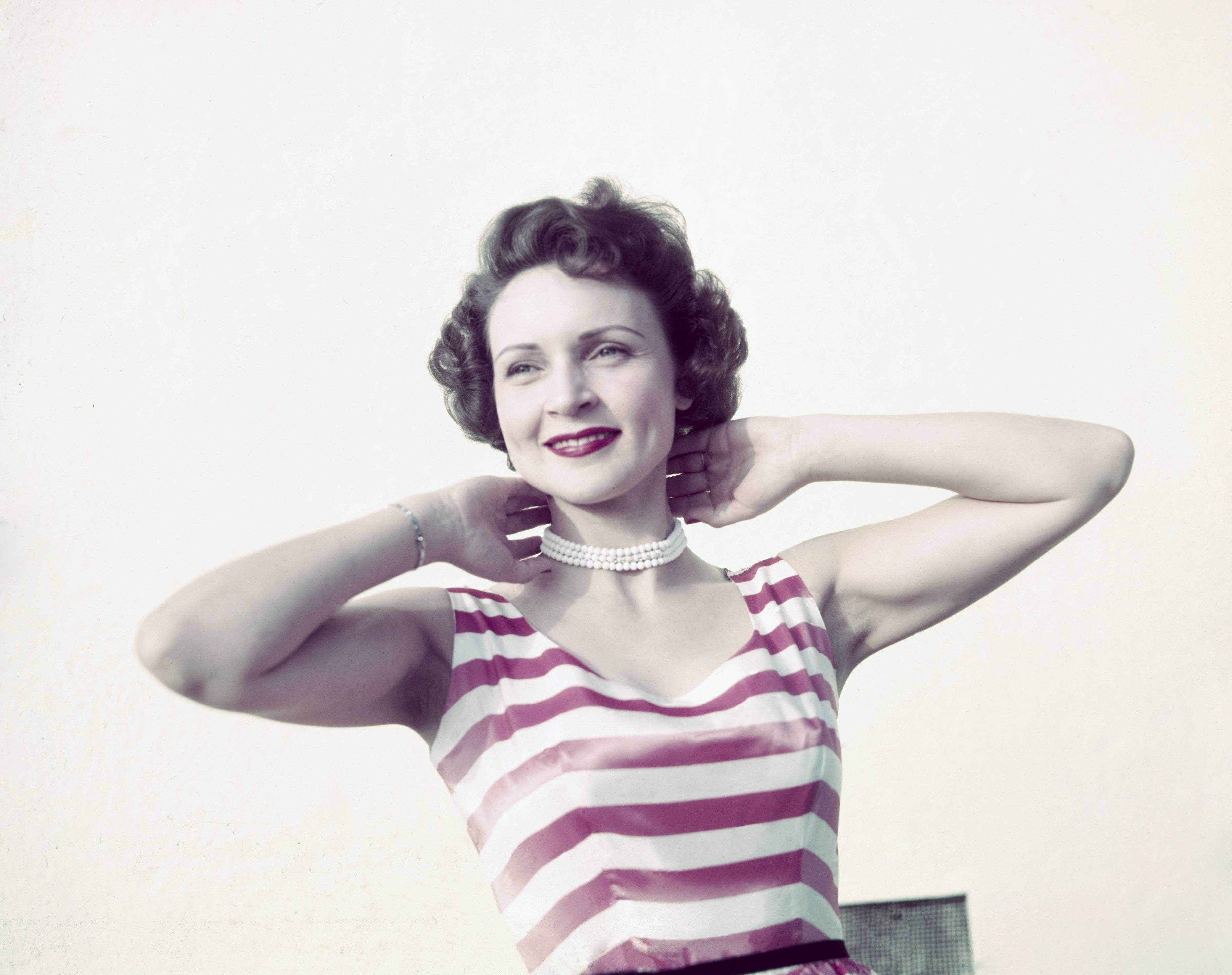 Betty White 桌布 壁紙 — 一位微笑女士穿著粉白條紋連衣裙，雙手放在頸後擺姿勢的復古肖像。