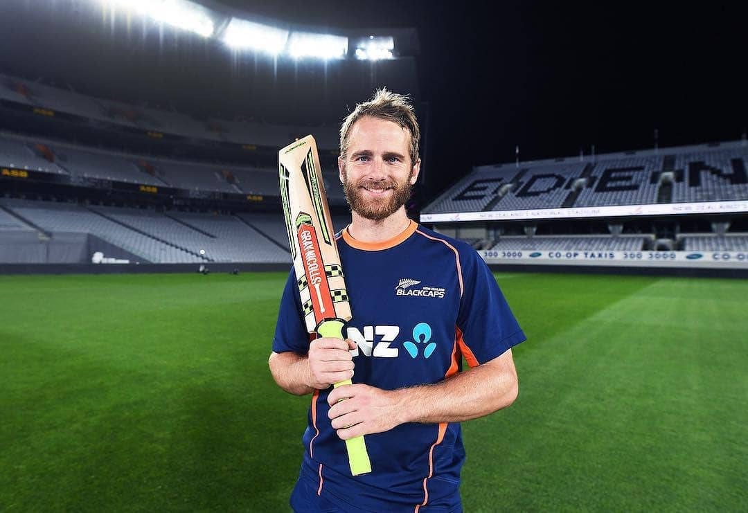 kane williamson 桌布 壁紙 — 一位微笑留鬍鬚的板球運動員身穿紐西蘭黑帽隊球衣，在夜間燈光明亮的球場上手持板球拍。