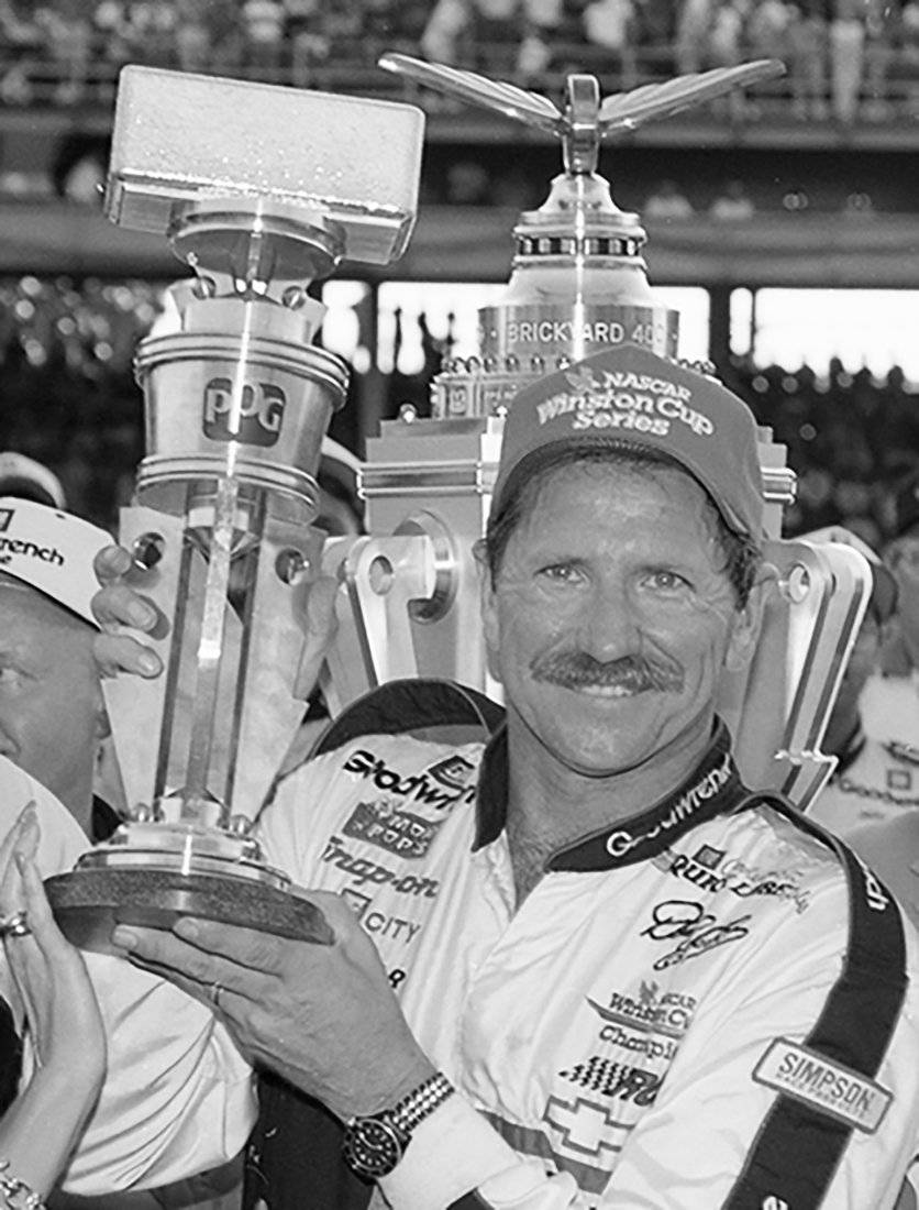 Victory 桌布 壁紙 — 一位微笑的NASCAR車手在黑白賽車勝利慶祝活動中自豪地舉起兩個大獎盃。