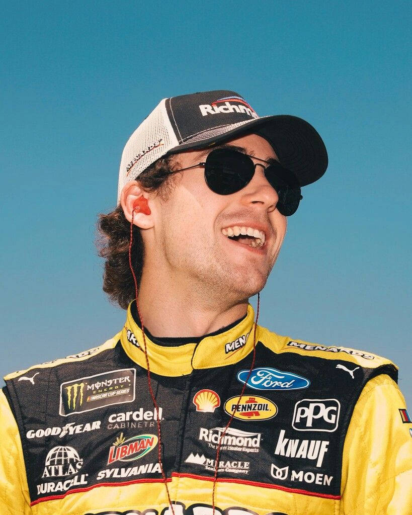 Ryan Blaney 桌布 壁紙 — 一位微笑的NASCAR車手穿著黃黑賽車服，帶有贊助商標誌，在晴朗的藍天下。