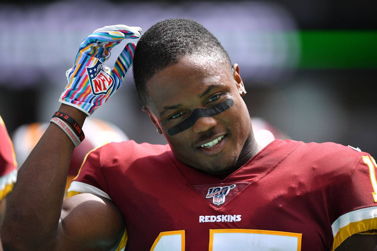 Football Players 桌布 壁紙 — 一位微笑的NFL美式足球員，身穿紅色球衣和彩色手套，在陽光明媚的比賽中觸摸頭部。