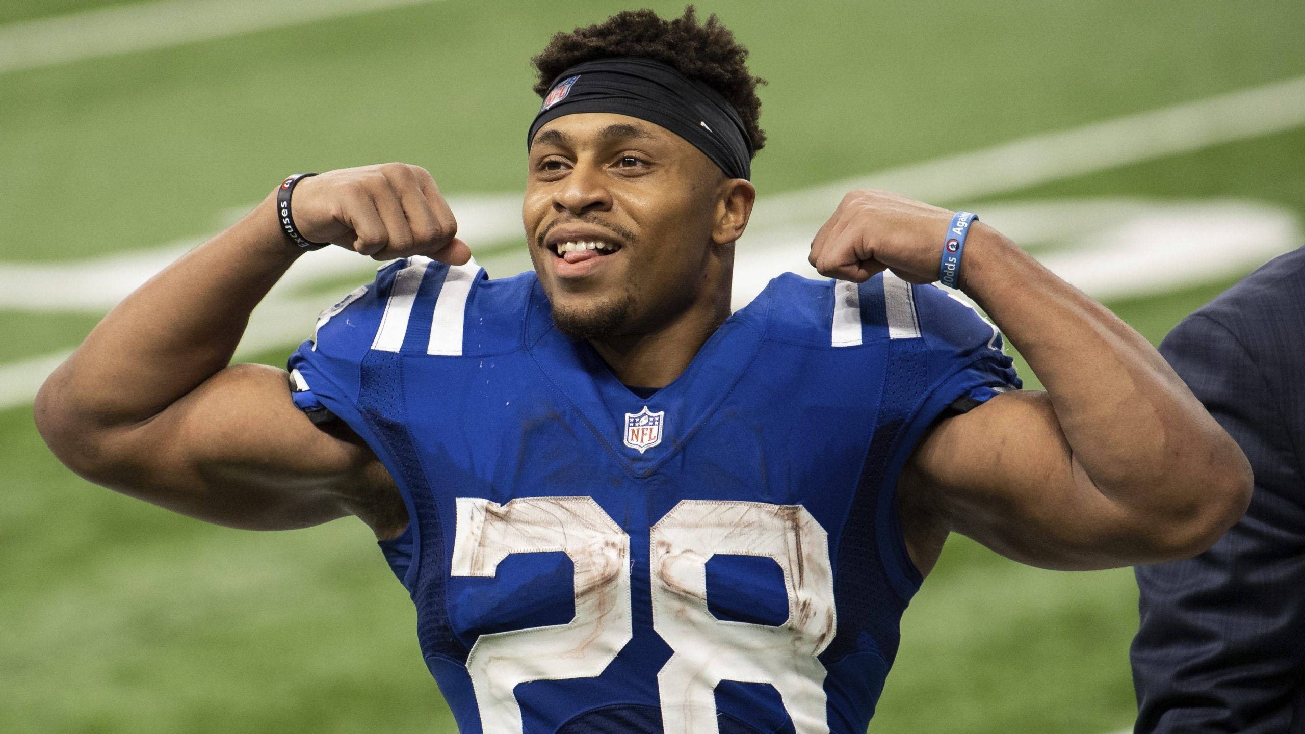 Jonathan 桌布 壁紙 — 一位微笑的NFL美式足球員身穿藍色球衣，在綠色球場上彎曲雙臂。