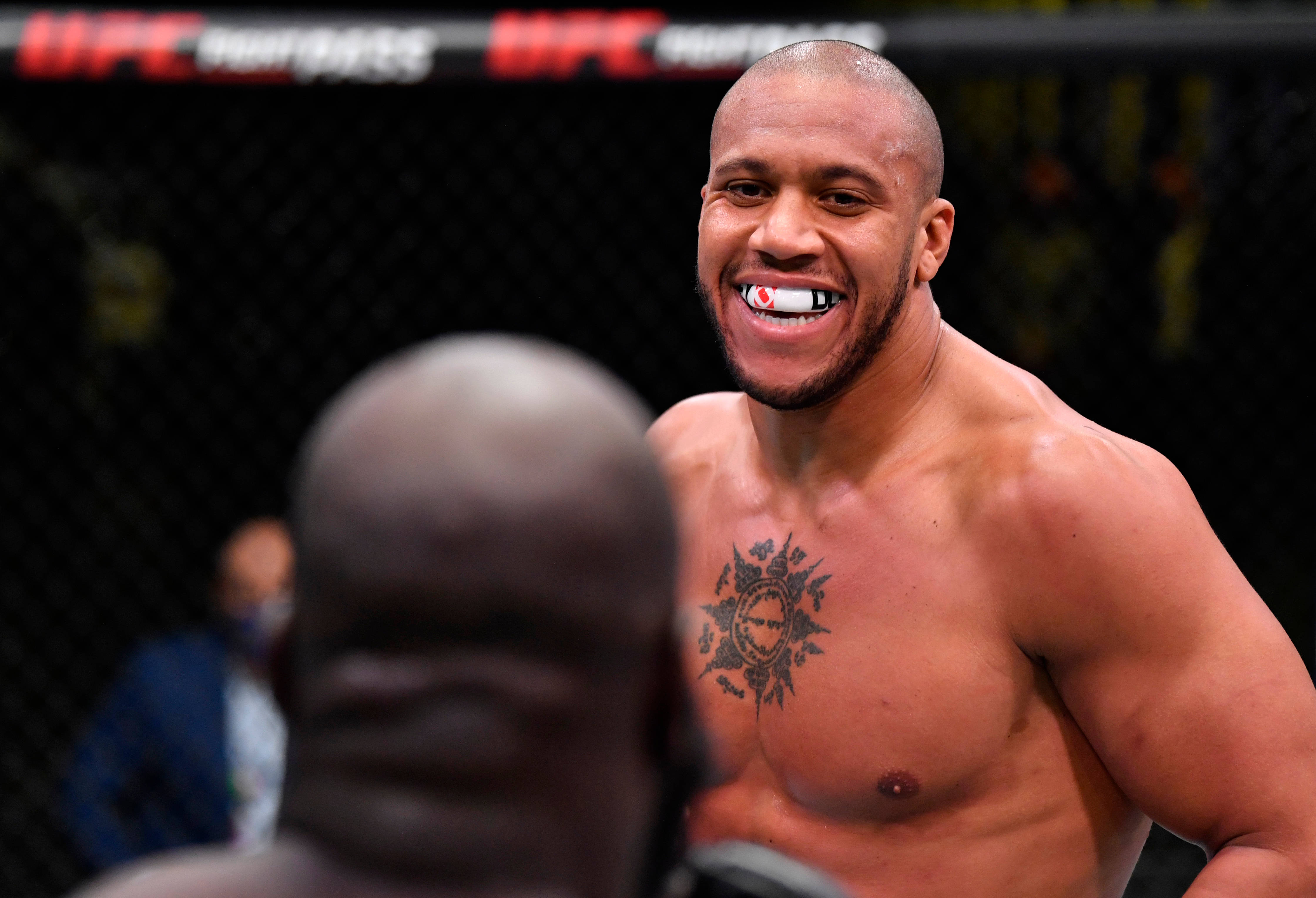 MMA 桌布 壁紙 — 一位微笑的UFC拳手，胸口有刺青，戴著護齒，在八角籠內面對他的對手。