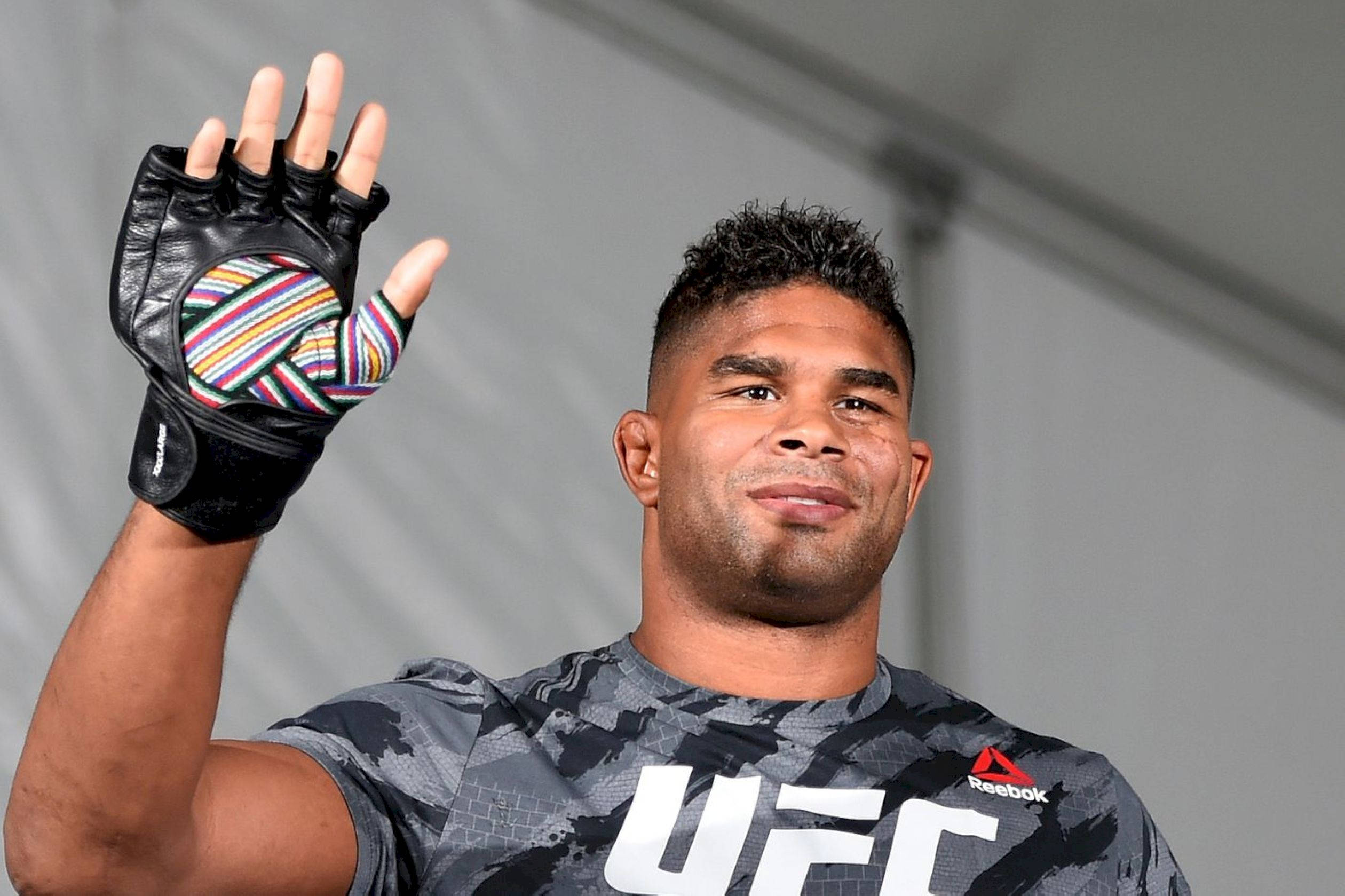 UFC 桌布 壁紙 — 一位微笑的UFC拳手在純灰色背景下揮舞著色彩繽紛的條紋手套。