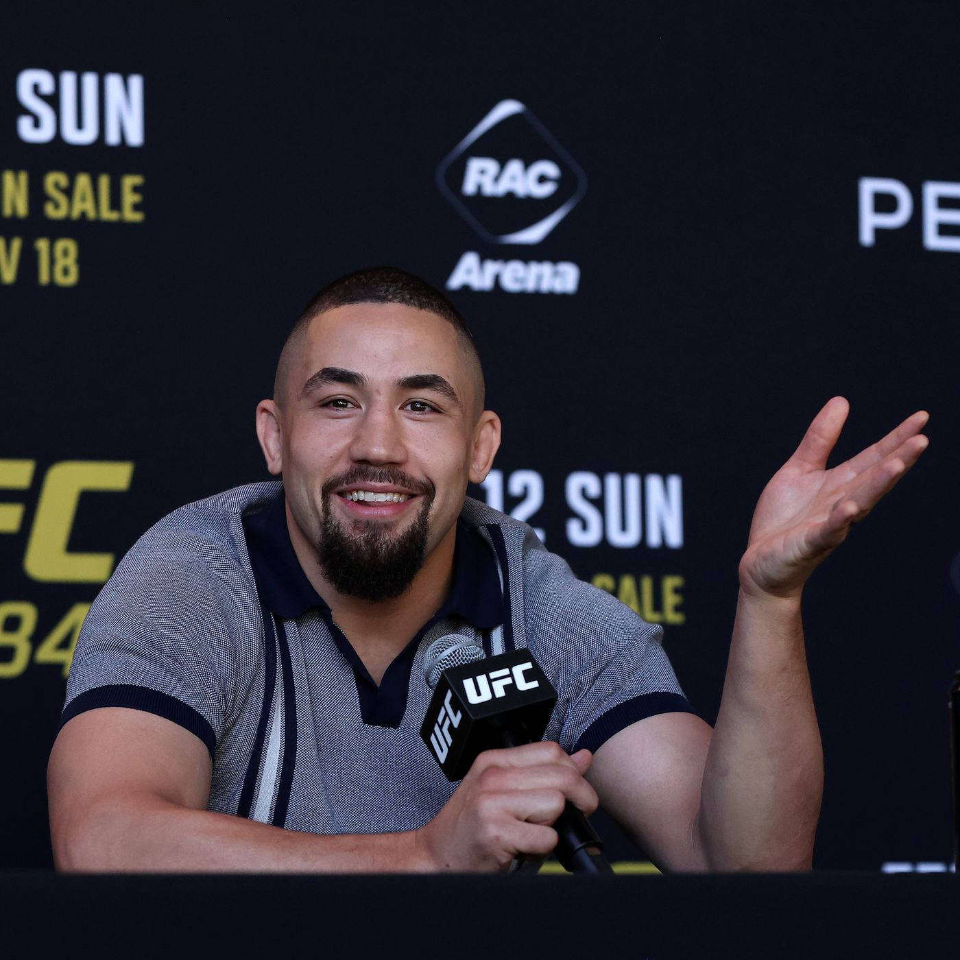 UFC 桌布 壁紙 — 一位微笑的UFC拳手在記者會上對著麥克風說話並做手勢，背景有品牌標誌。