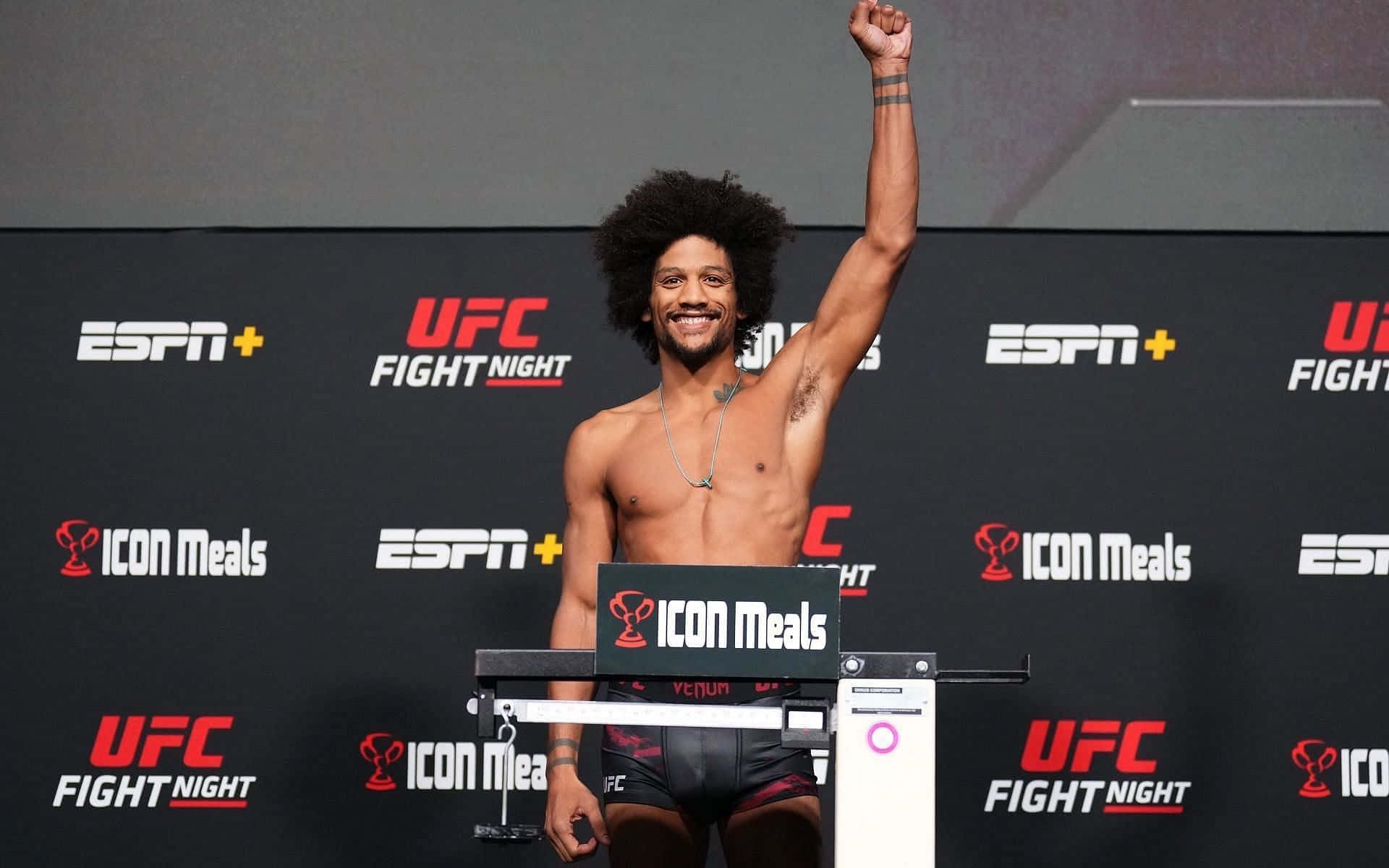 MMA 桌布 壁紙 — 一位微笑的UFC拳手留著爆炸頭，在稱重活動中勝利地舉起拳頭站在體重秤上。