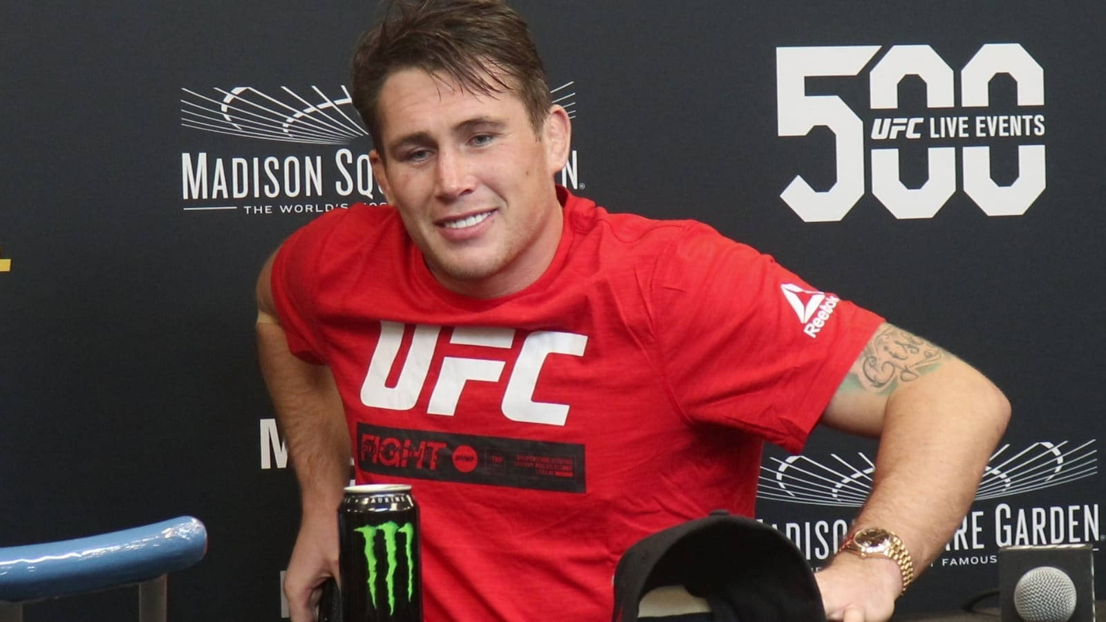UFC 桌布 壁紙 — 一位微笑的UFC拳手穿著紅色品牌T恤，在'Madison Square Garden'和'500 UFC Live Events'背景的新聞活動中擺姿勢。