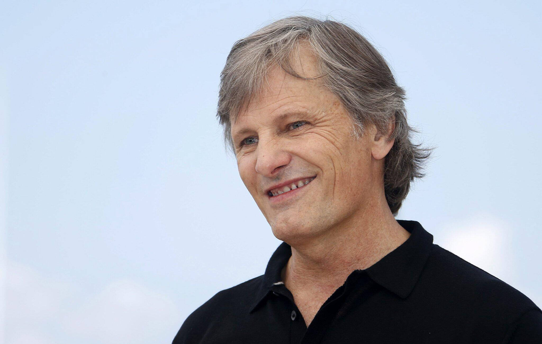actor 桌布 壁紙 — 一位微笑的中年灰髮男子穿著黑色Polo衫，以柔和藍天為背景的特寫肖像。