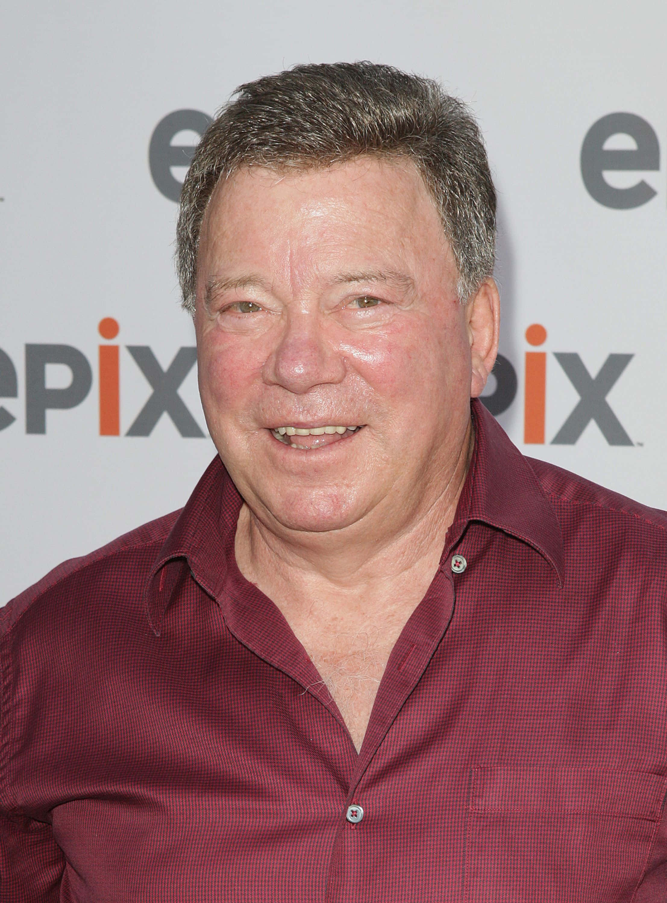 william shatner 桌布 壁紙 — 一位微笑的中年男子身穿栗色格紋襯衫，站在白色Epix品牌背景前。