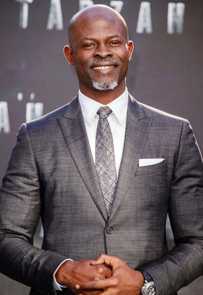 Celebrity 桌布 壁紙 — 一位微笑的光頭男士，身穿灰色西裝和圖案領帶，自信地站在電影首映背景前。