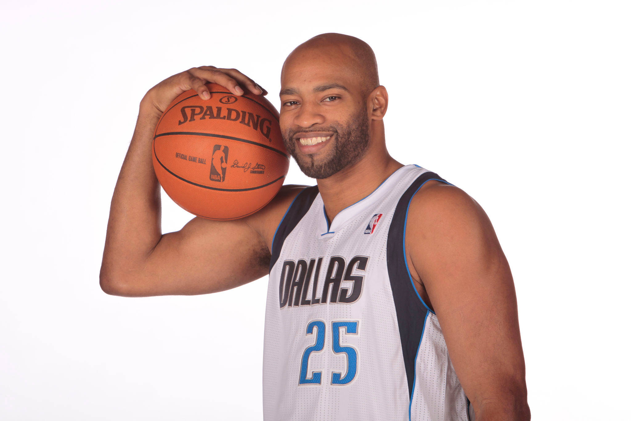 NBA 桌布 壁紙 — 一位微笑的光頭籃球運動員穿著達拉斯球衣，在純白背景上拿著一個Spalding球。