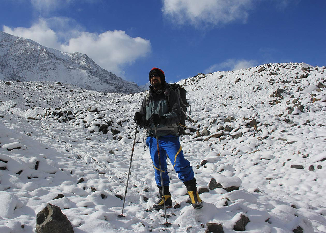 Climbing 桌布 壁紙 — 一位微笑的冬季裝備徒步旅行者站在白雪覆蓋的岩石山坡上，天空湛藍，雲朵蓬鬆。