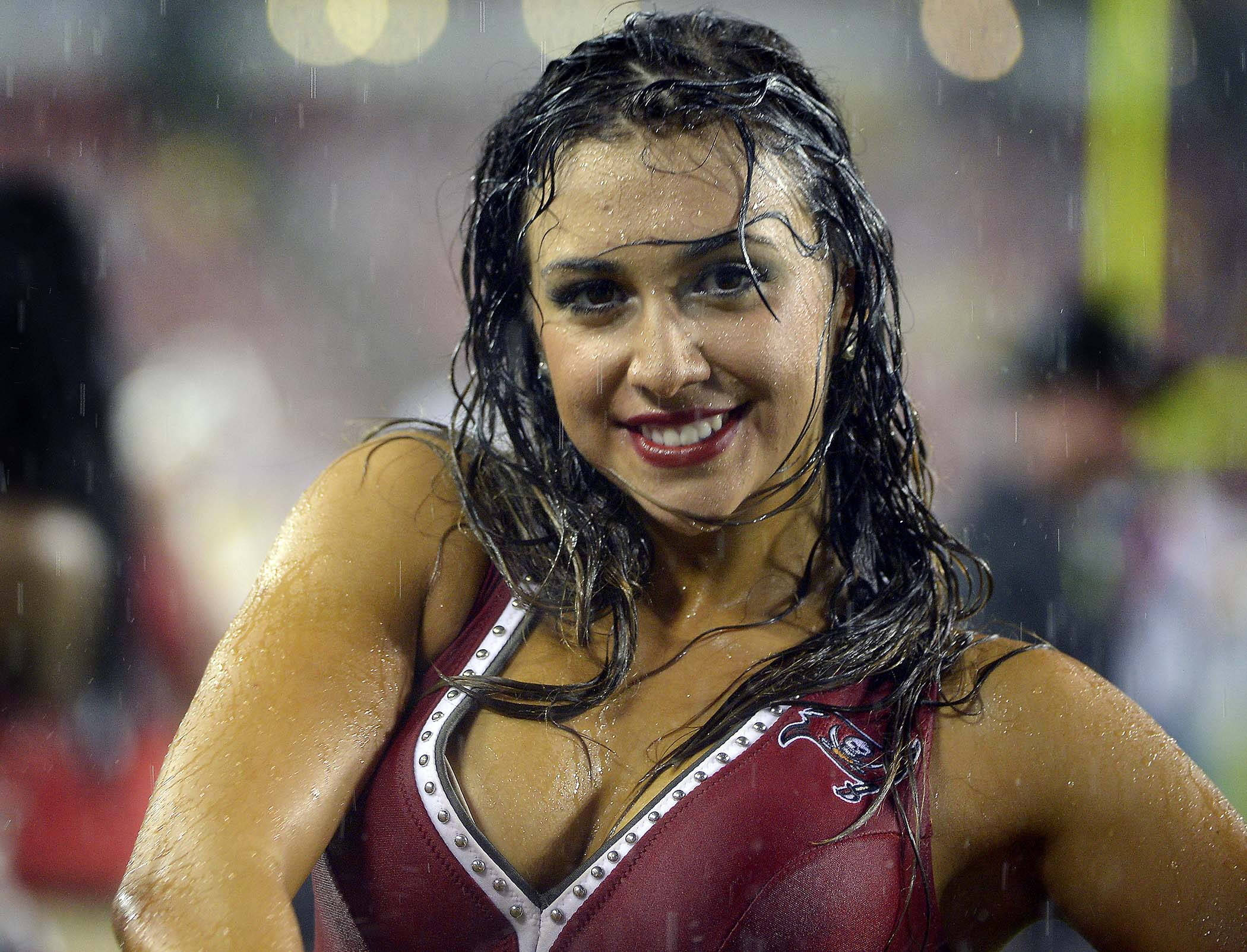 Cheerleader 桌布 壁紙 — 一位微笑的啦啦隊員，濕髮濕膚，在夜間體育場活動中站在雨中。