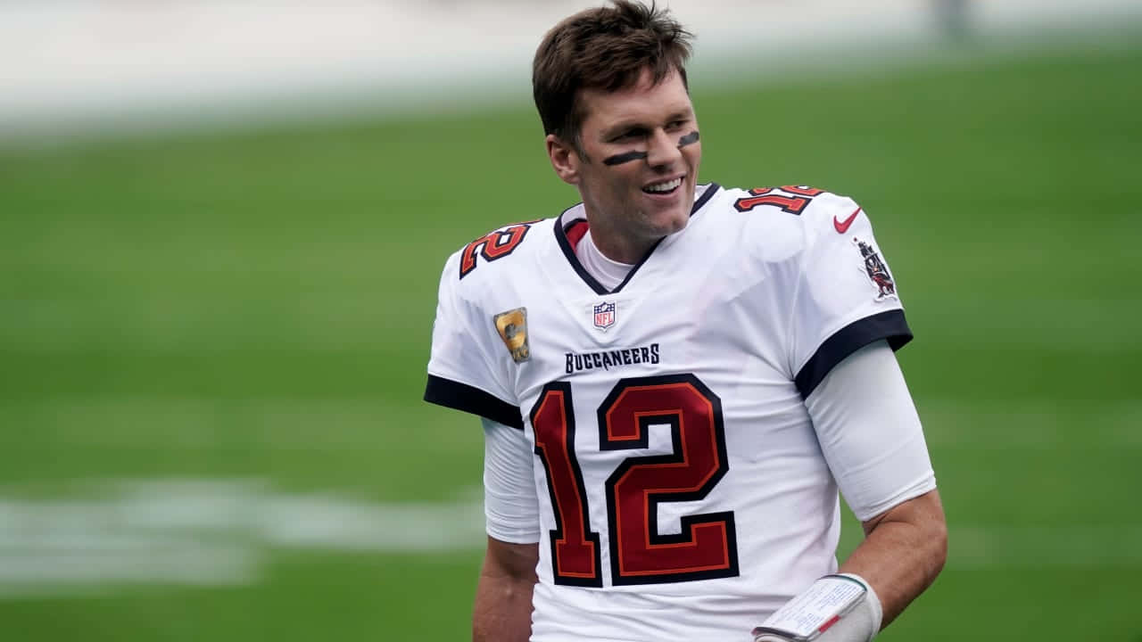 NFL 桌布 壁紙 — 一位微笑的坦帕灣海盜隊四分衛，身穿白色12號球衣，站在綠色足球場上。