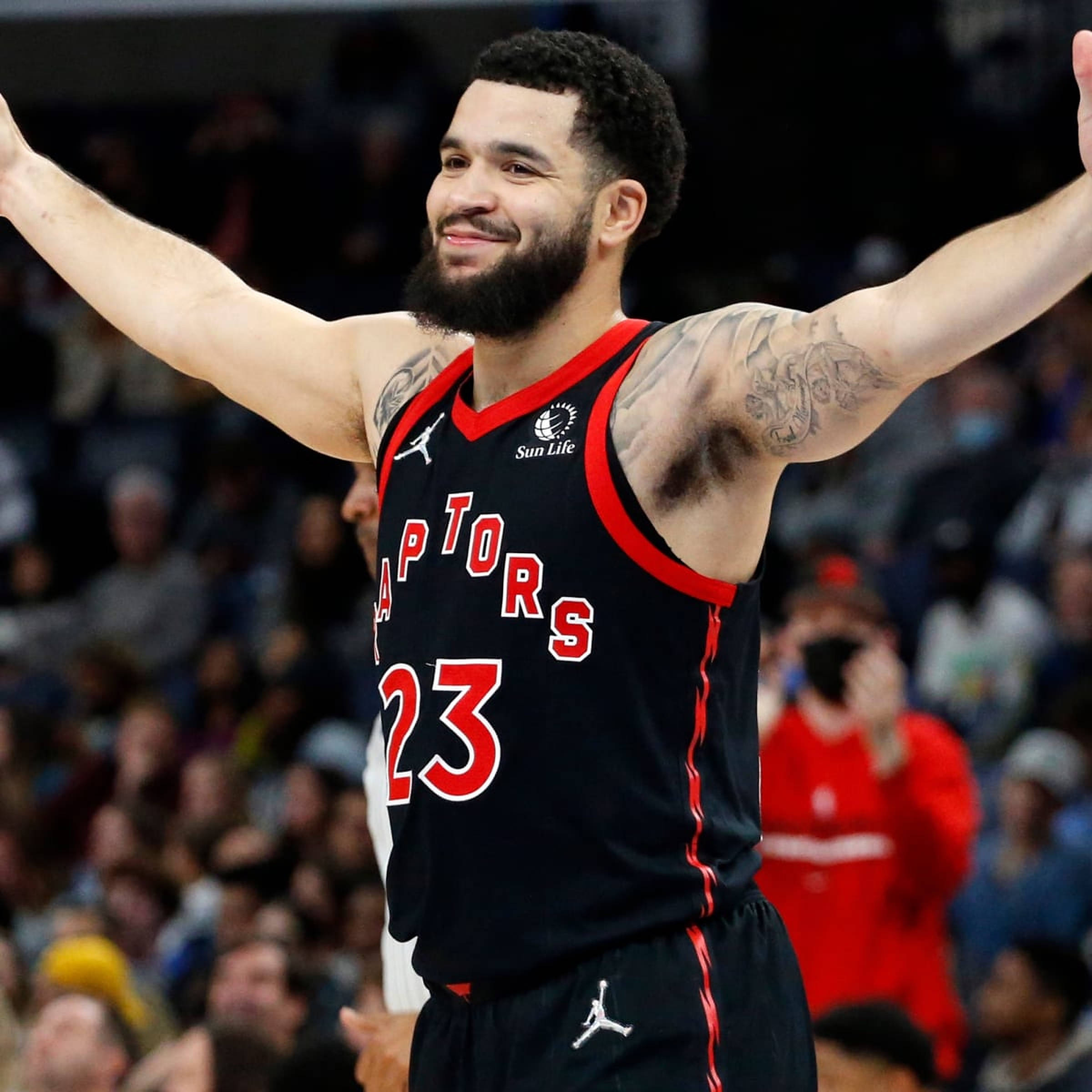 Fred Vanvleet 桌布 壁紙 — 一位微笑的多倫多暴龍籃球運動員高舉雙臂，在擠滿觀眾的場館中慶祝，身穿黑紅色球衣。