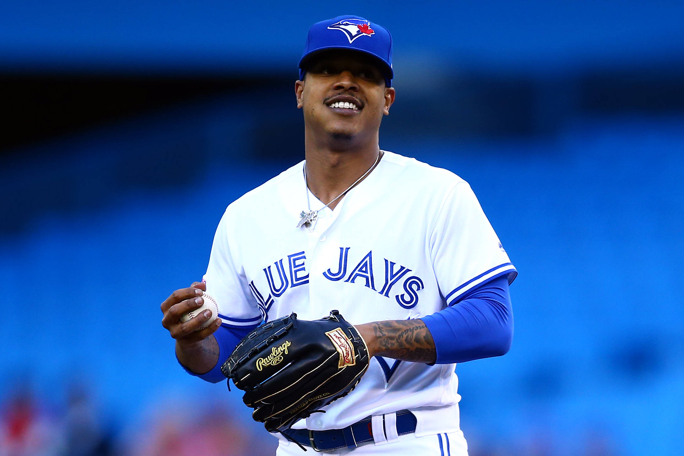 Marcus Stroman 桌布 壁紙 — 一位微笑的多倫多藍鳥隊棒球運動員，手持棒球和手套，背景是模糊的藍色球場。