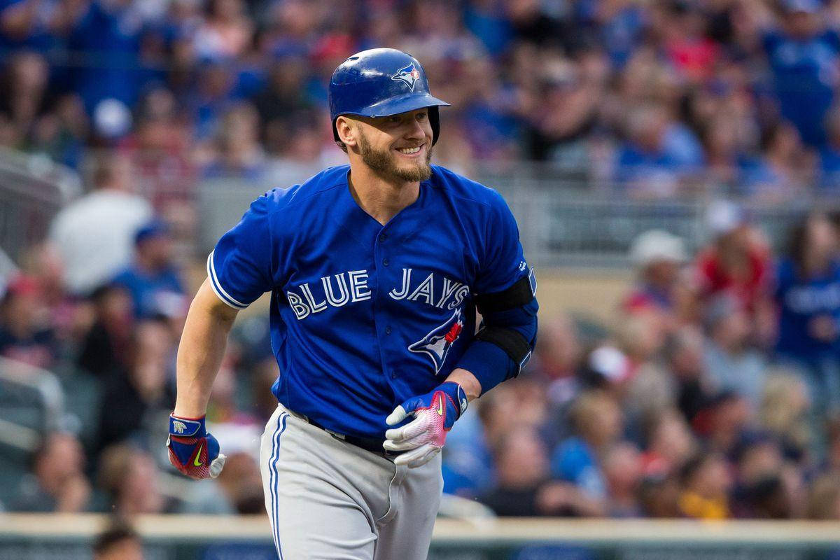 MLB 桌布 壁紙 — 一位微笑的多倫多藍鳥隊棒球運動員身穿藍色制服，在陽光明媚的球場上奔跑，背景是歡呼的人群。